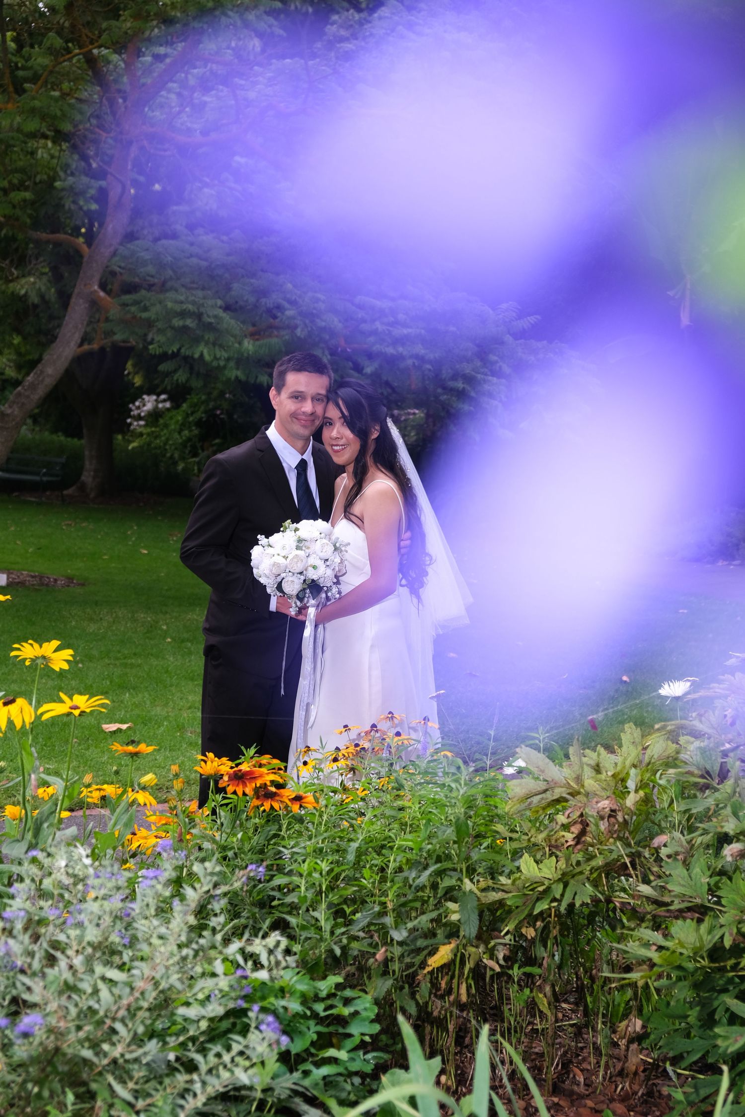 Bride and groom embracing in a lush garden surrounded by colorful wildflowers and greenery.