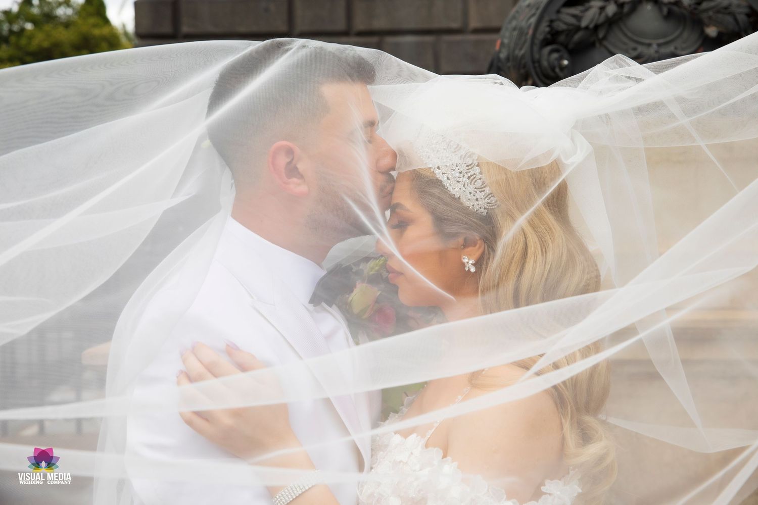 Bride and groom sharing a tender kiss beneath a flowing white veil during their wedding ceremony.