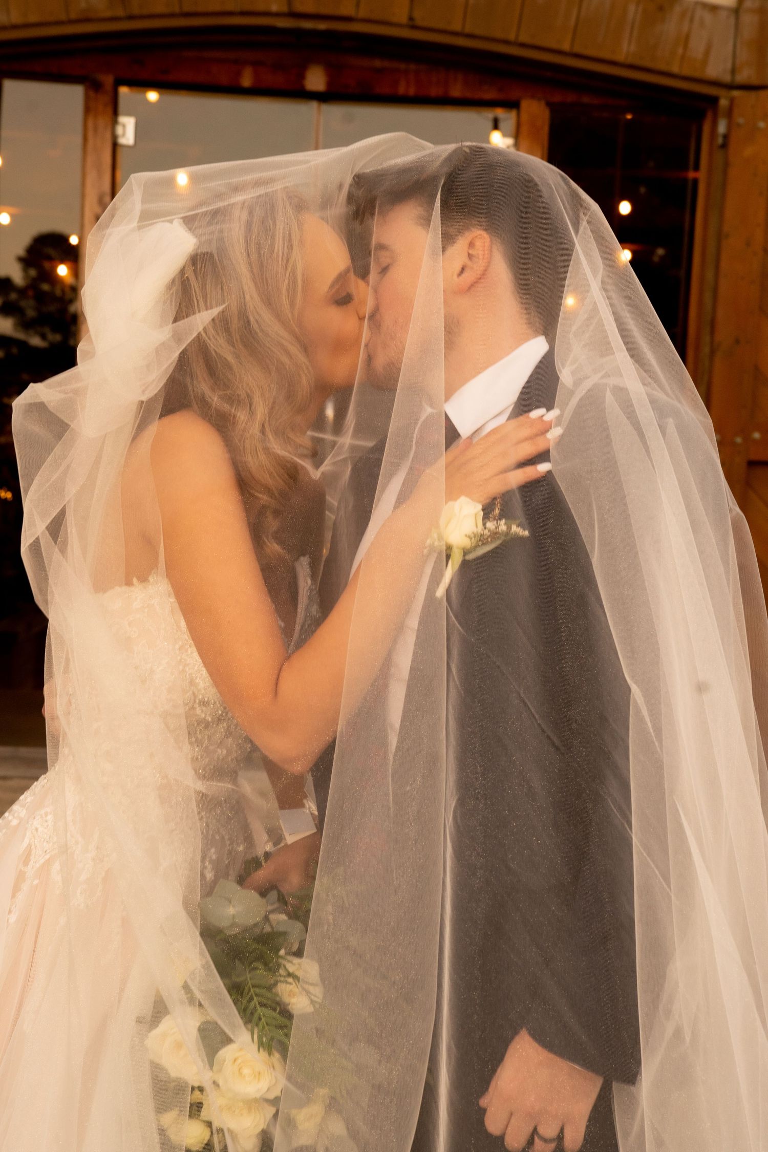 Bride and groom sharing romantic kiss hidden beneath flowing white wedding veil.