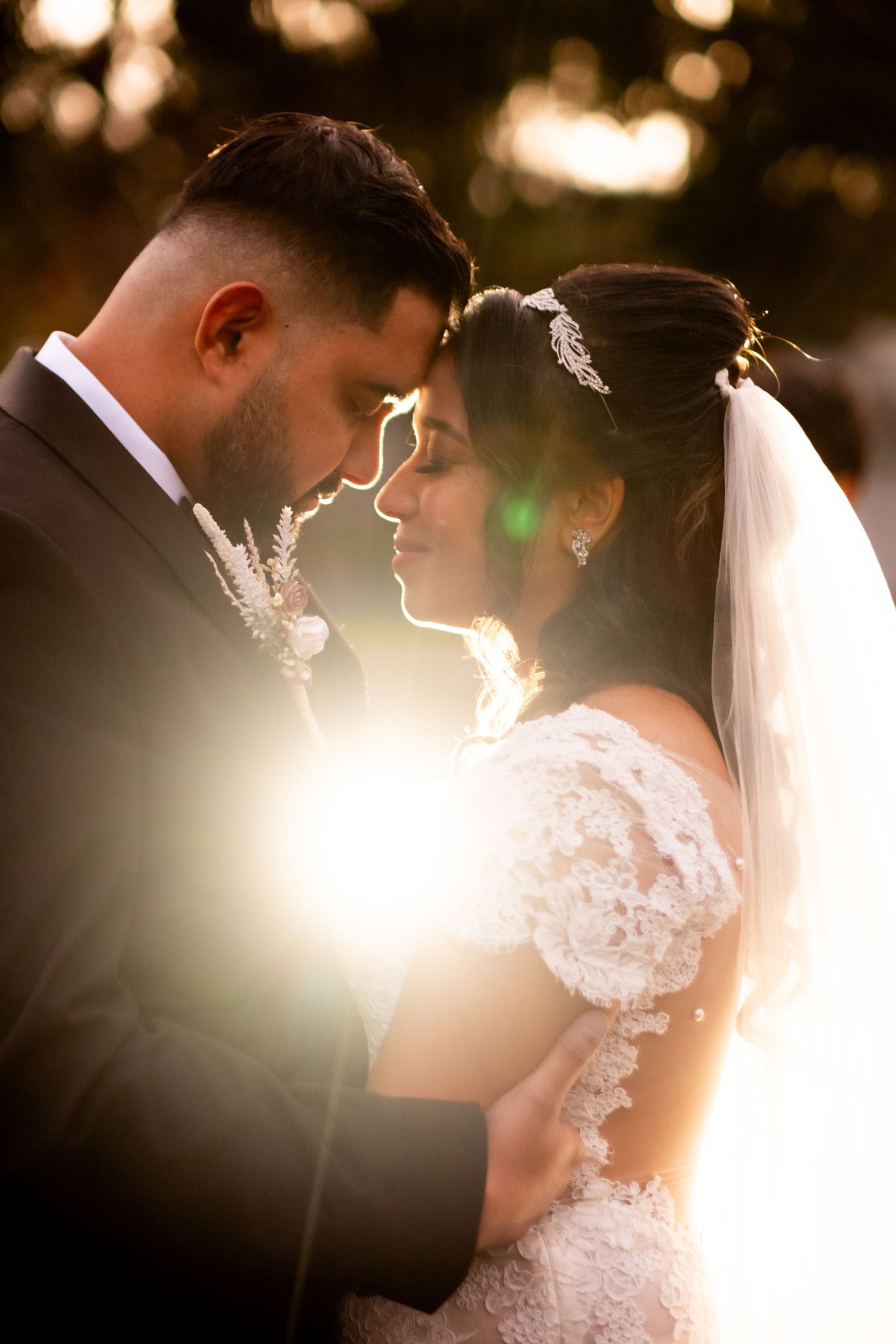 Bride and groom touch foreheads in golden sunset light during romantic outdoor wedding portrait.