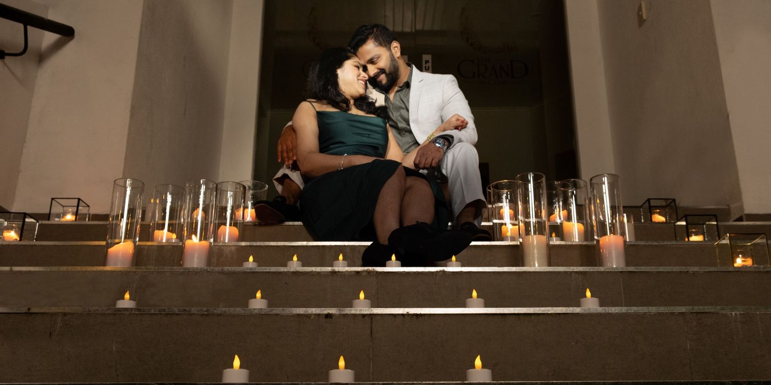 Romantic couple sitting on candlelit steps surrounded by glowing tea light candles in elegant setting.
