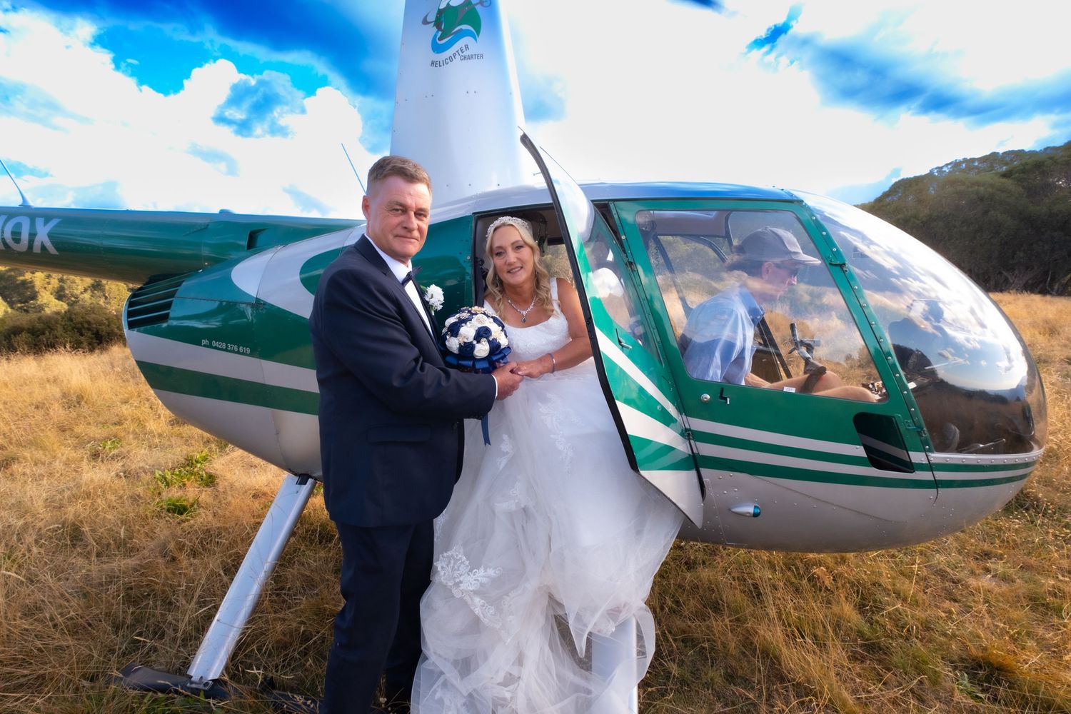 Happy bride and groom posing in front of green helicopter on sunny day.