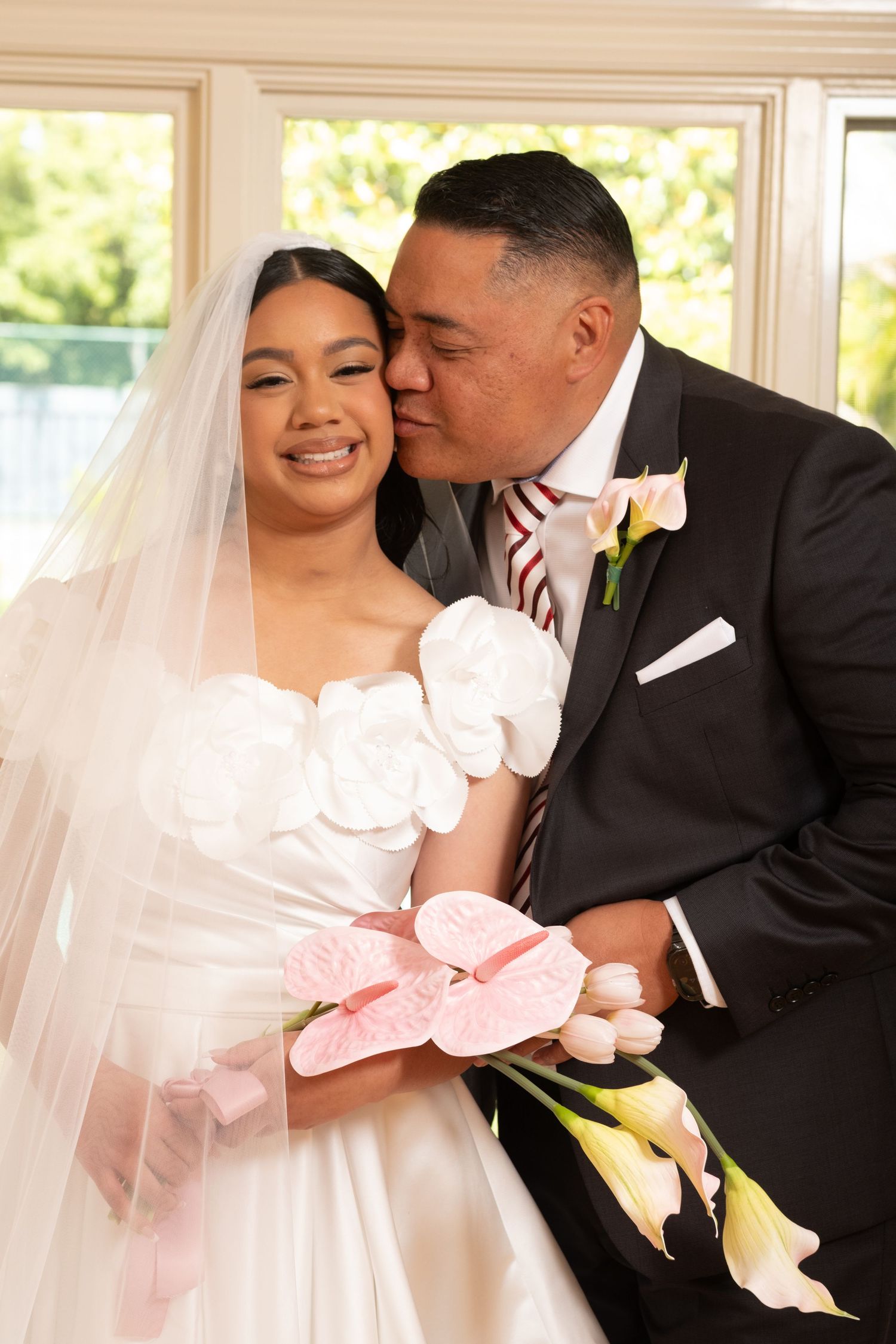 Father of the bride kisses her cheek while she holds a pink tropical bouquet.