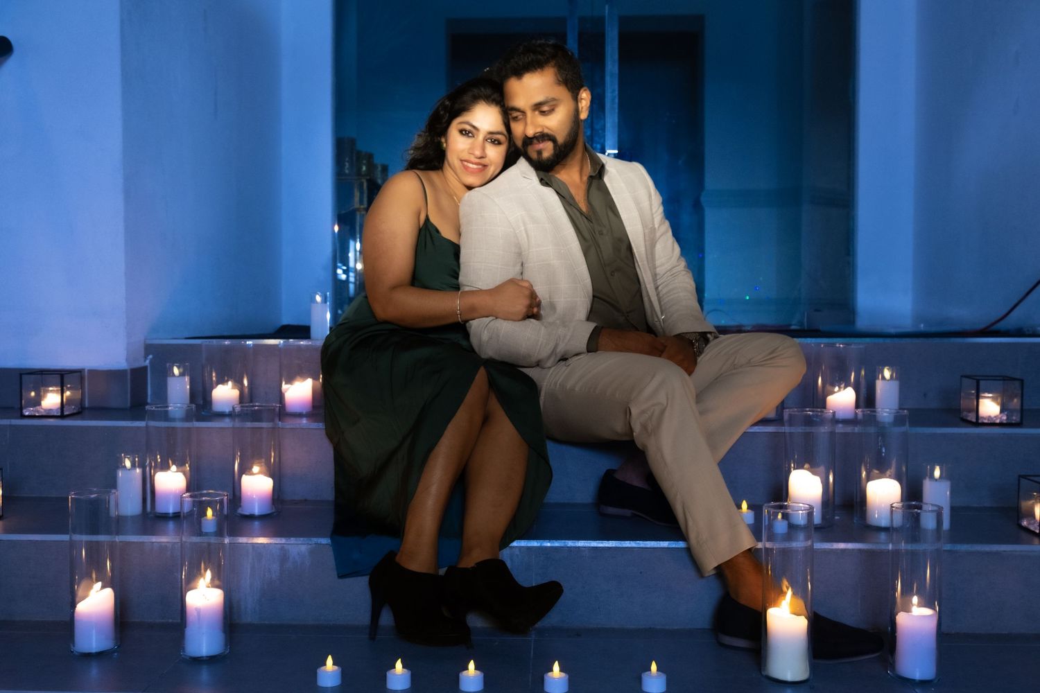 Romantic couple sits together on candlelit steps in soft blue evening light during engagement session.