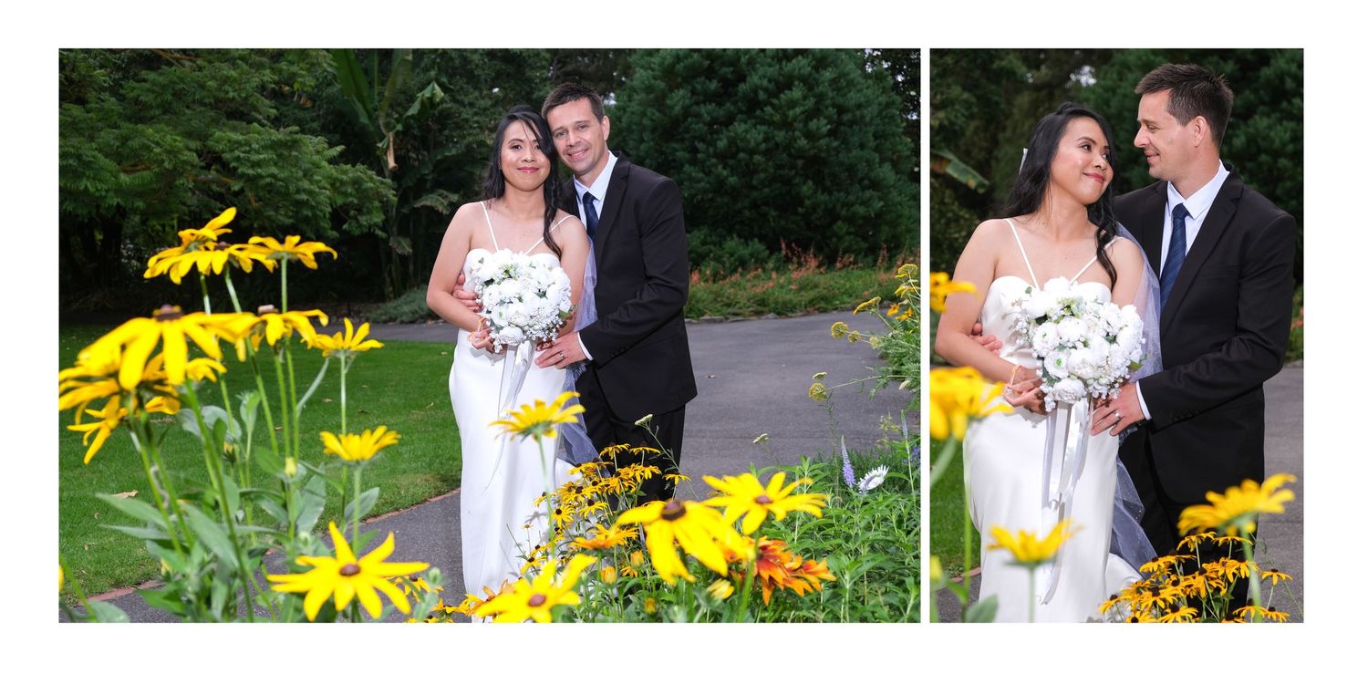 A bride and groom pose together smiling among bright yellow flowers in a lush garden setting.