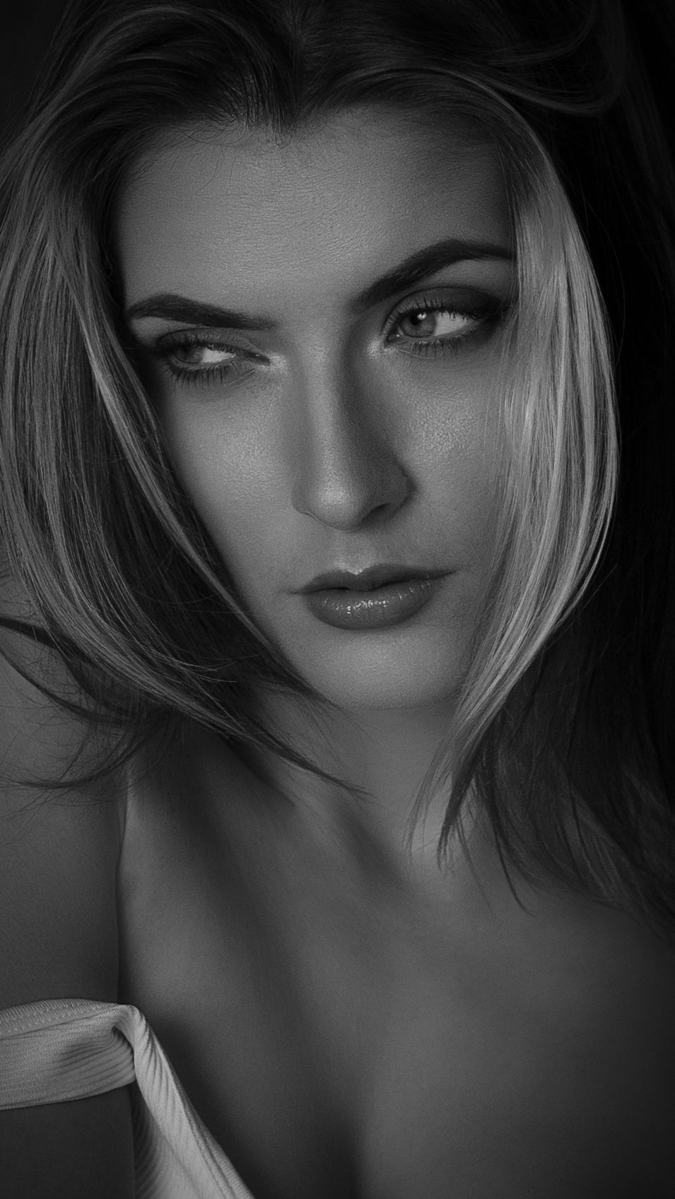 Black and white portrait of a young woman with bold makeup and flowing hair, gazing intensely at the camera.