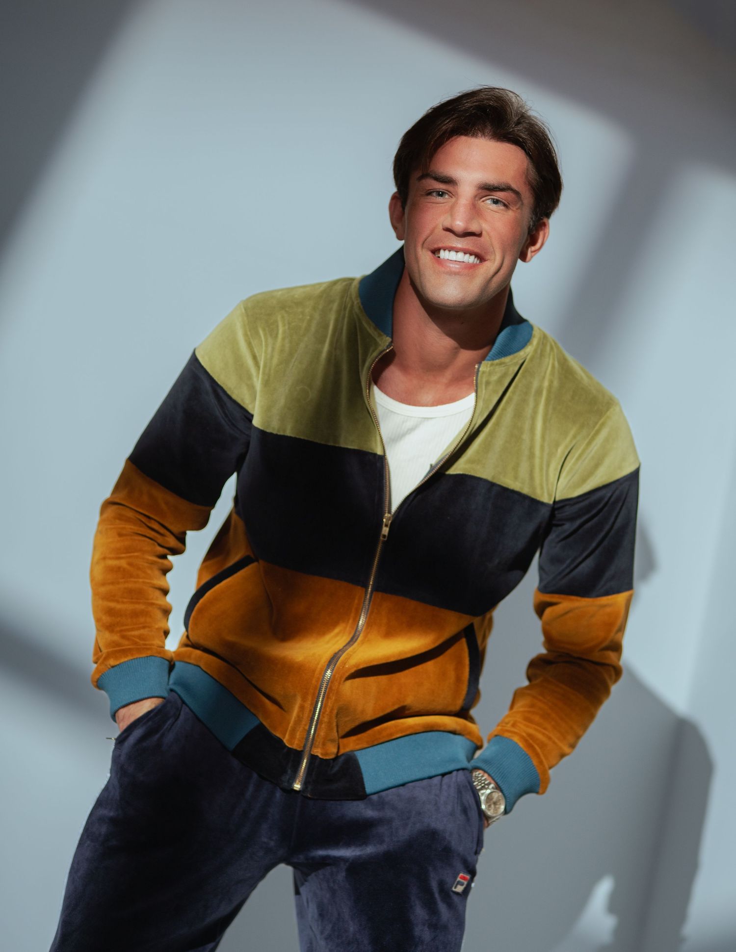 Smiling man wearing a colorful striped velour zip-up jacket in olive, navy, and amber with teal accents.