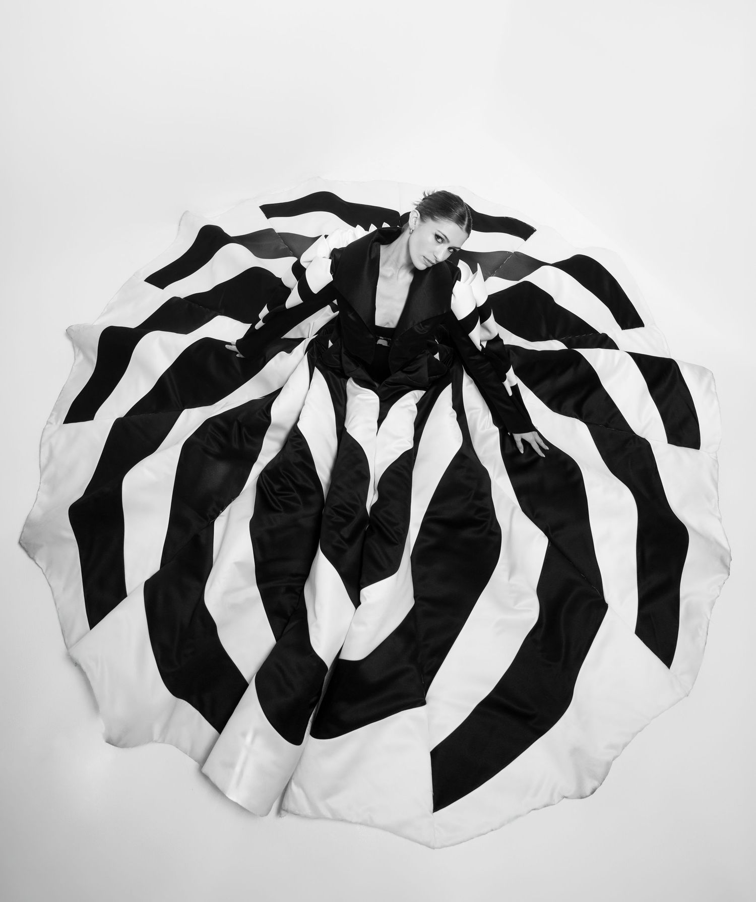 Aerial view of a model in a dramatic black and white striped ballgown spread wide, shot in monochrome.