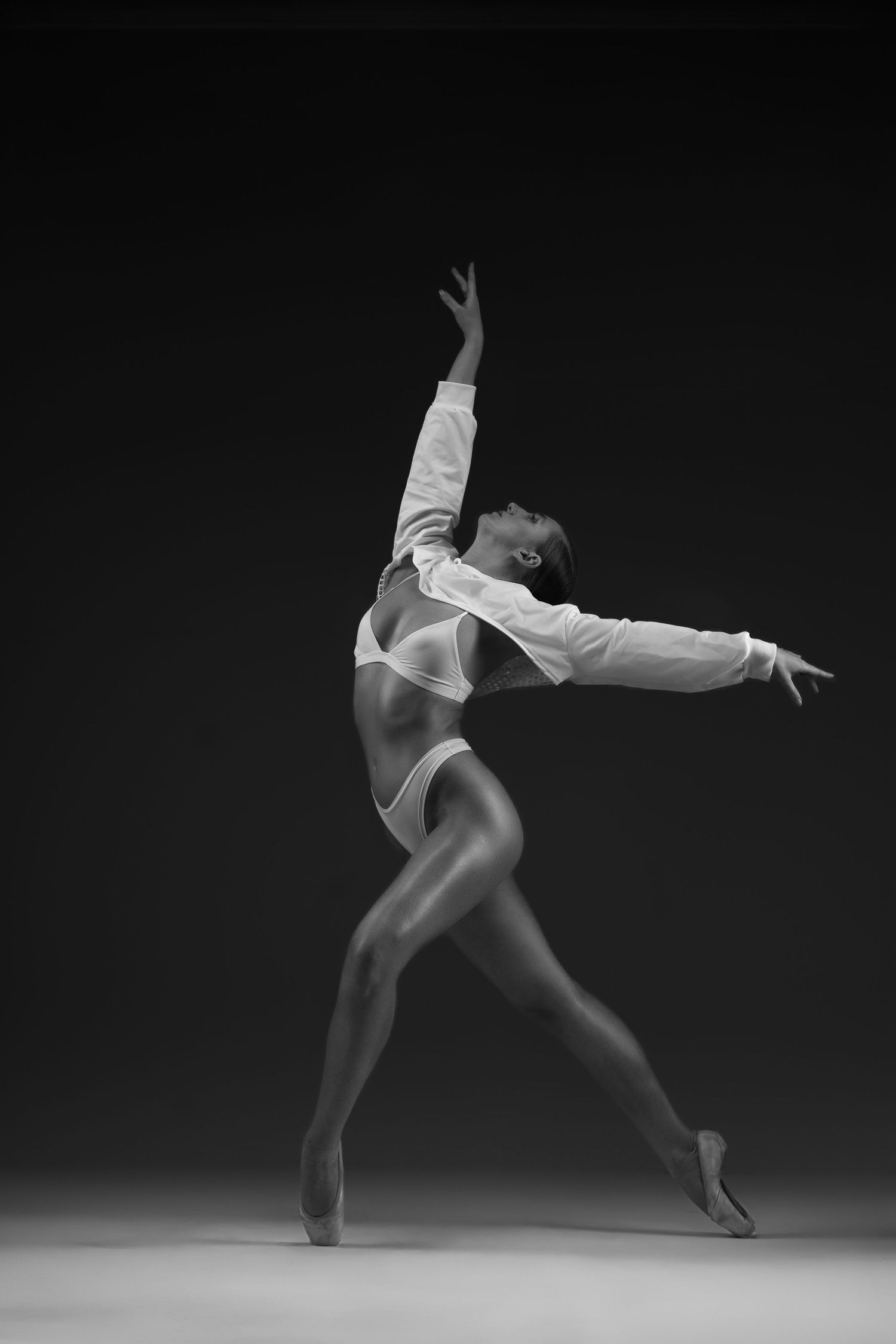 Black and white photo of a graceful ballet dancer in white outfit striking an elegant pose on pointe.