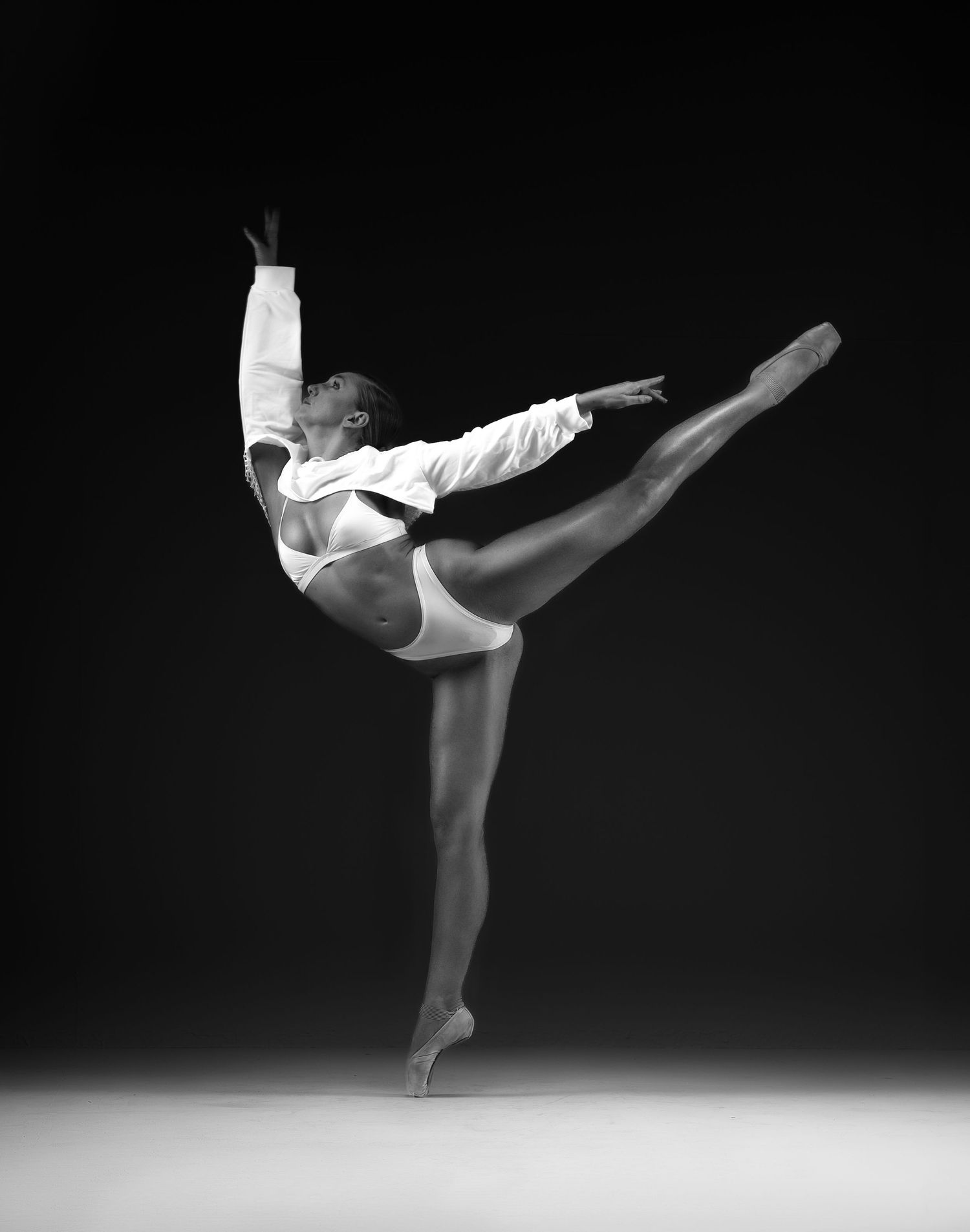 Black and white photo of a ballet dancer en pointe performing an arabesque with one arm raised gracefully.