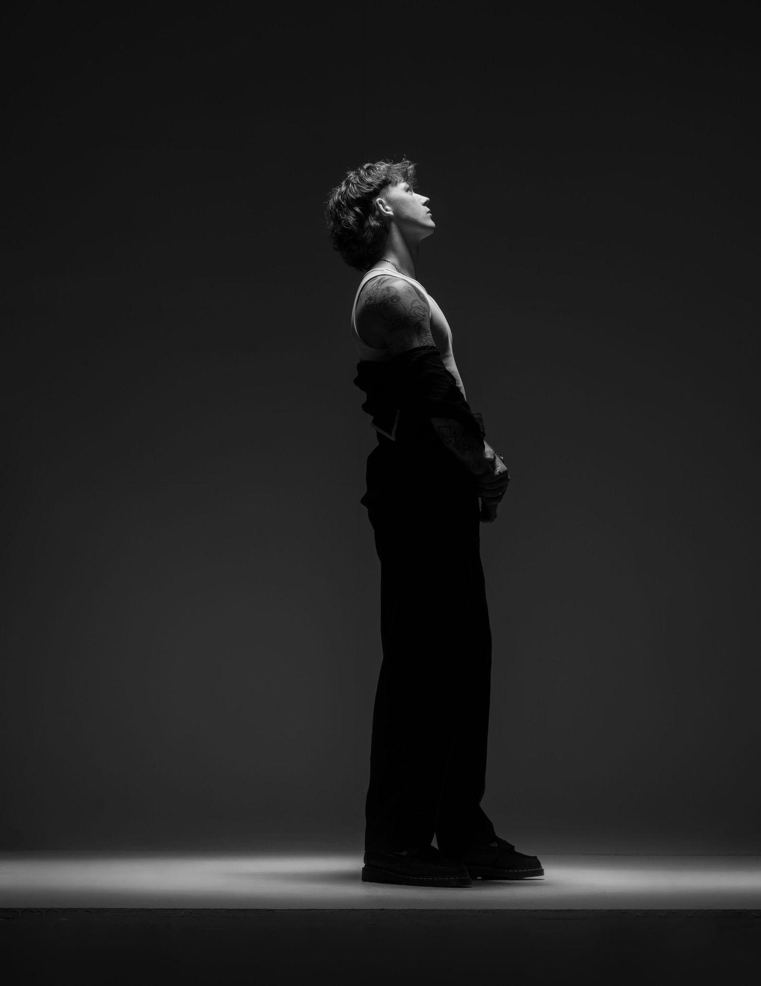Black and white profile portrait of a person standing tall with head raised, dramatic studio lighting.