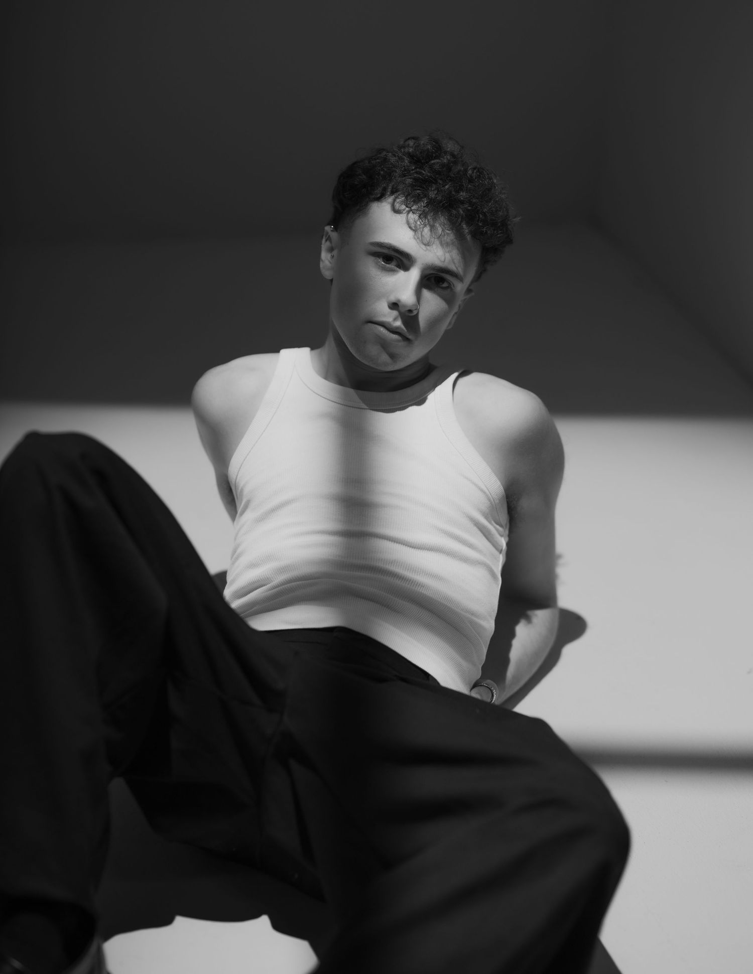 Black and white portrait of a young man in a white tank top and black trousers posing confidently.