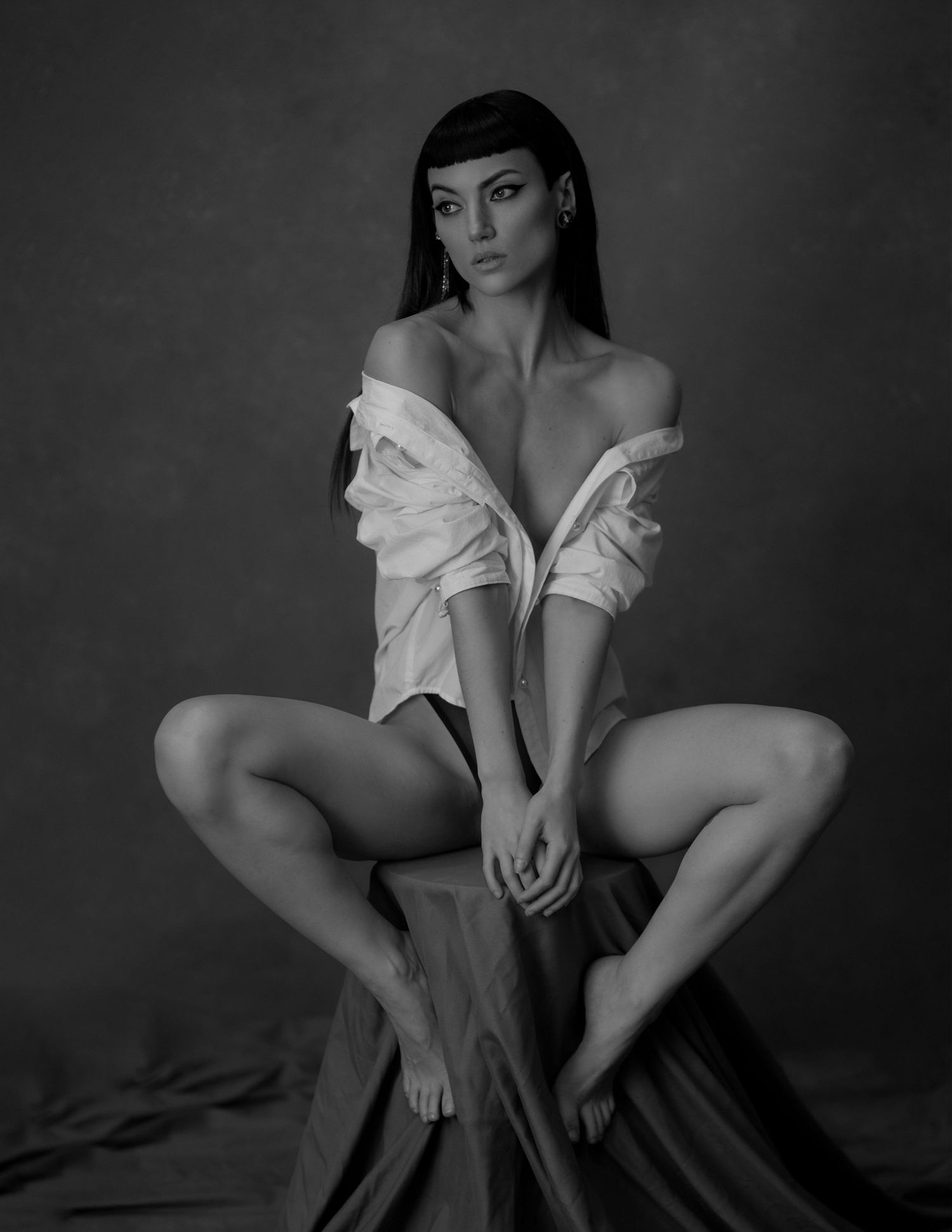 Black and white fine art portrait of a woman in an off-shoulder white shirt seated in an elegant pose.