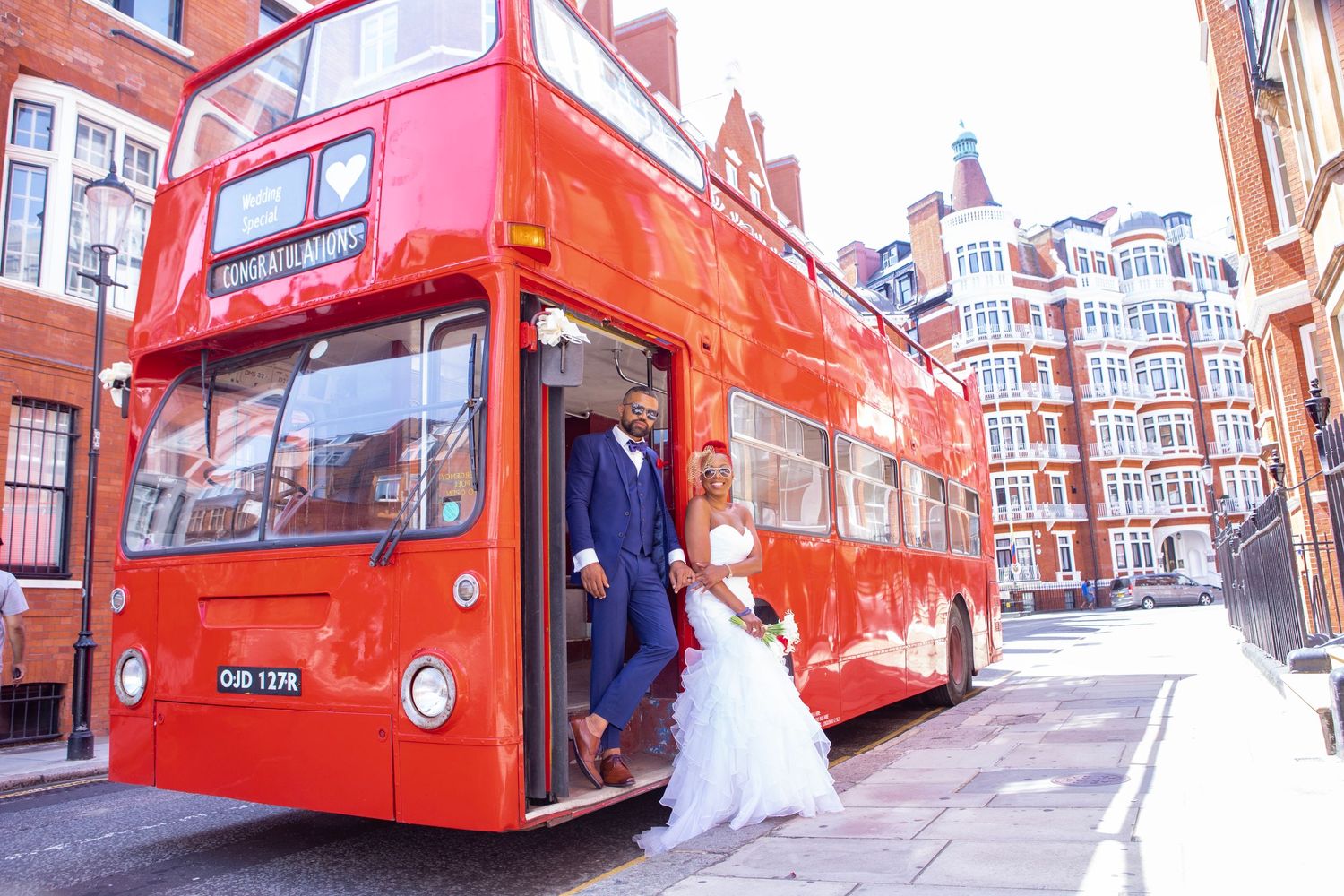 Wedding couple posing by red double decker bus on London street.
