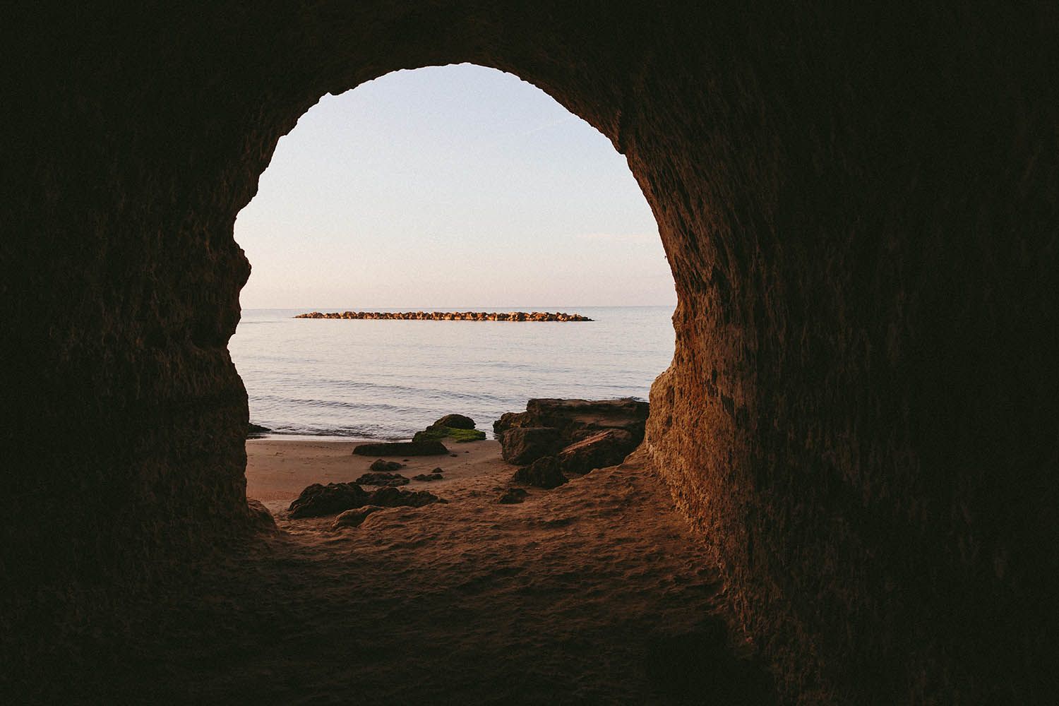 Color landscape photograph of the sea frames by a cave entrance in Anzio Italy with a small sand bar showing in the water taken at sunrise