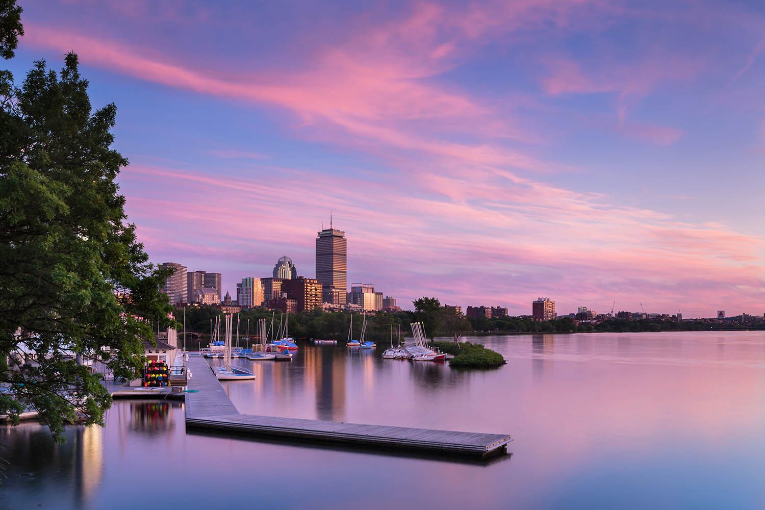 Color landscape photograph of Boston taken at dusk with the Charles River and pontoon floating with Boston skyline in distance
