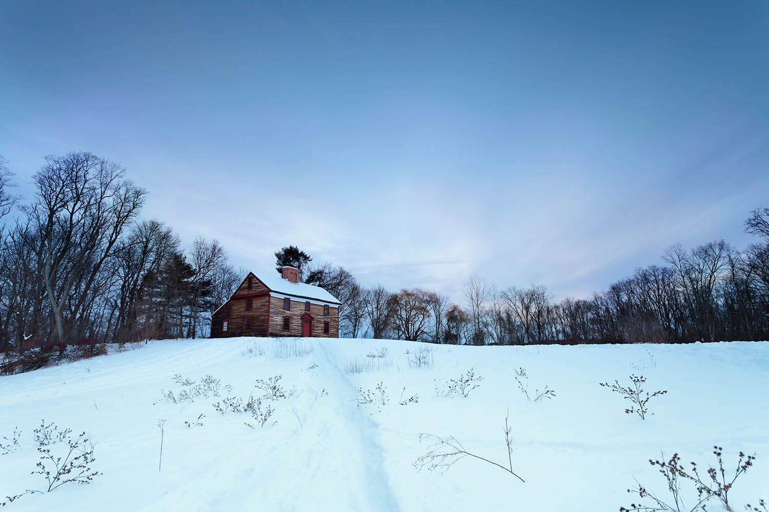 Color landscape photograph showing old historic house in Concord Massachusetts minuteman trail. House set in the snow at dusk.