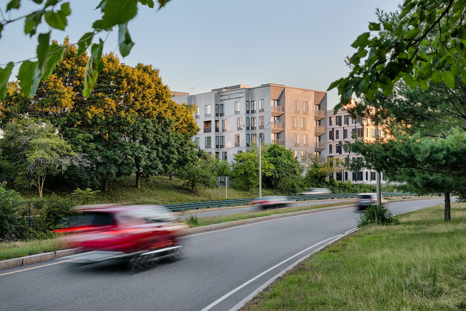 DUSK IMAGE OF BOSTON RESIDENTIAL COMPLEX TAKEN IN THE EVENING WITH A CAR DRIVING PAST BLURRED IN THE FOREGROUND