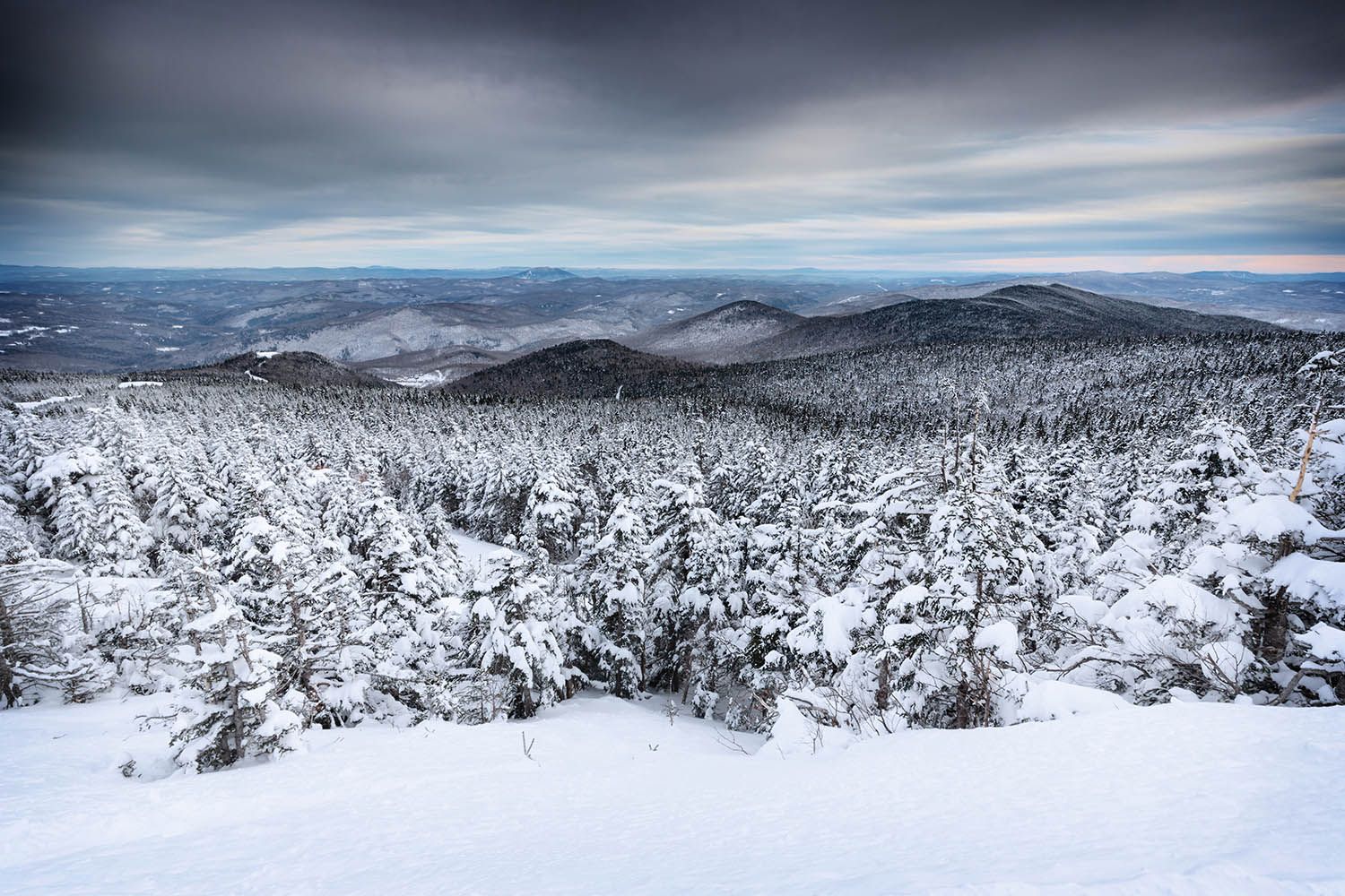 Color landscape photograph showing a wintery scene from Killington in Vermont taken from the ski trail with the mountains in the distance.