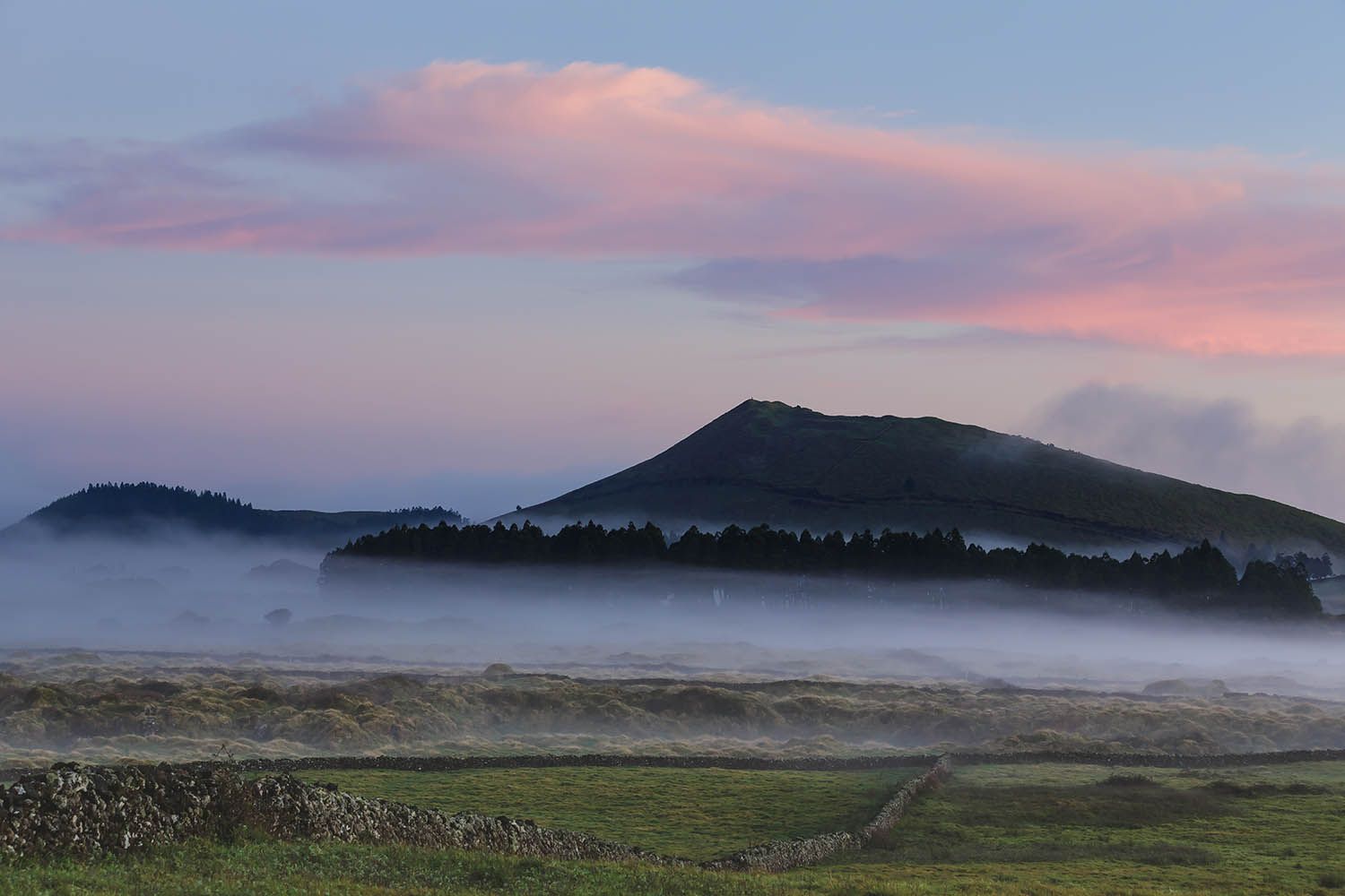 Color landscape photograph of Terceira Island in the Azores Portugal, showing the fog hanging around the base of mountain at dusk