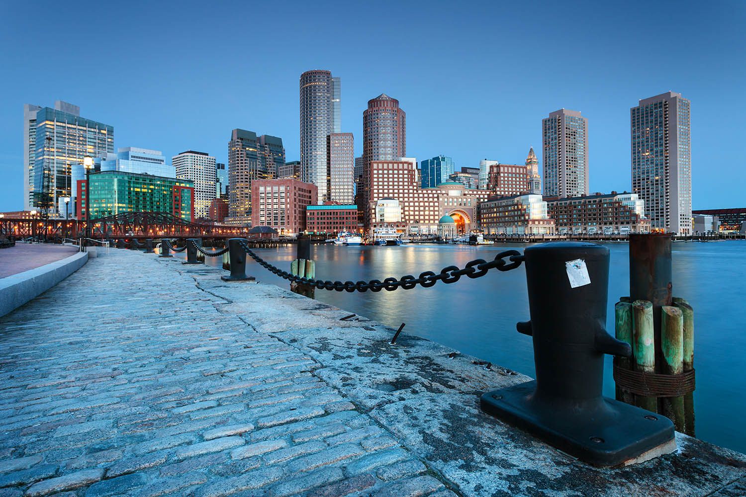 A classic color landscape image of the Boston skyline from the Seaport District with main buildings showing and harbor in foreground