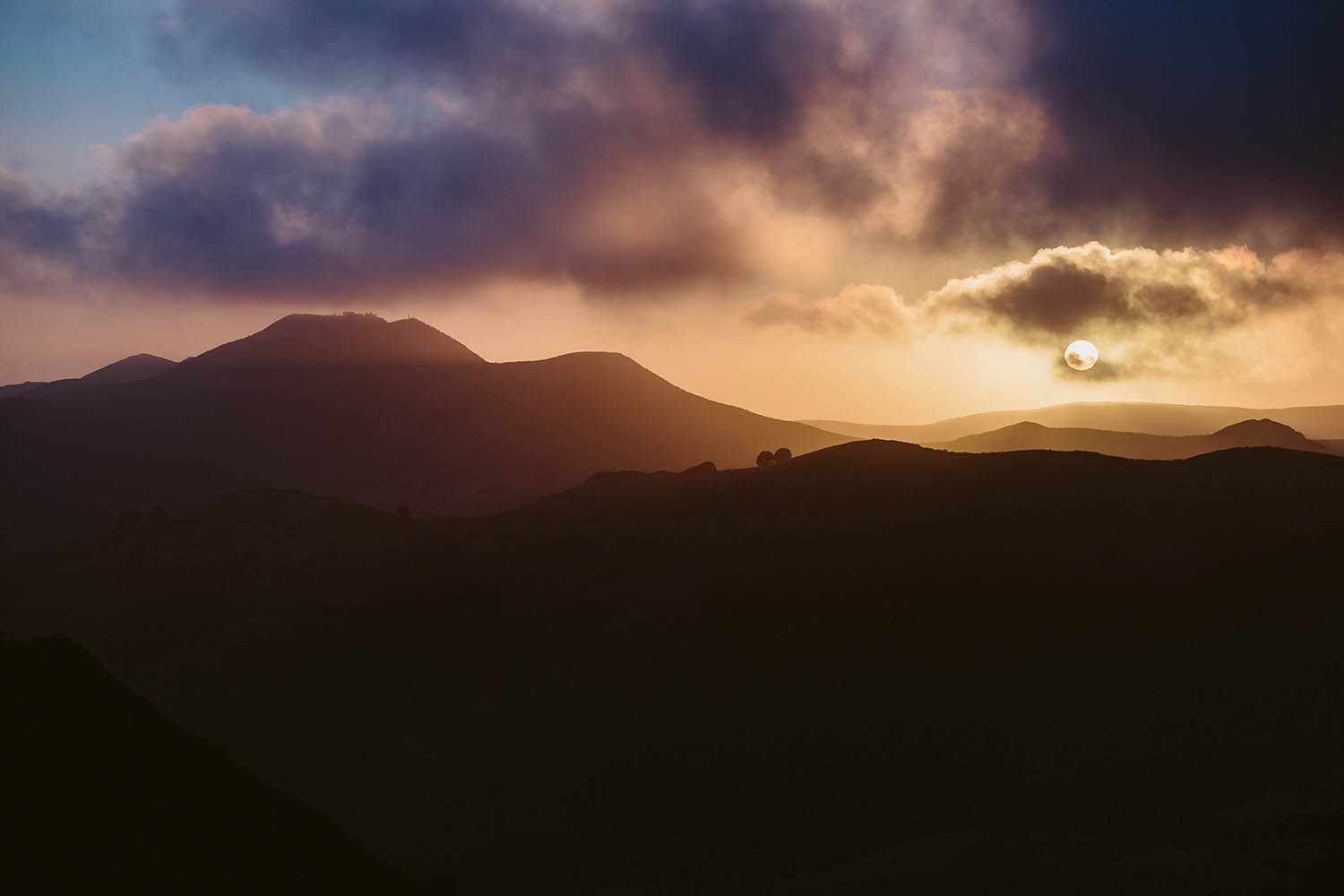 Color landscape photograph taken near San Francisco in California showing mountains with the sunsetting behind and sun beams through clouds