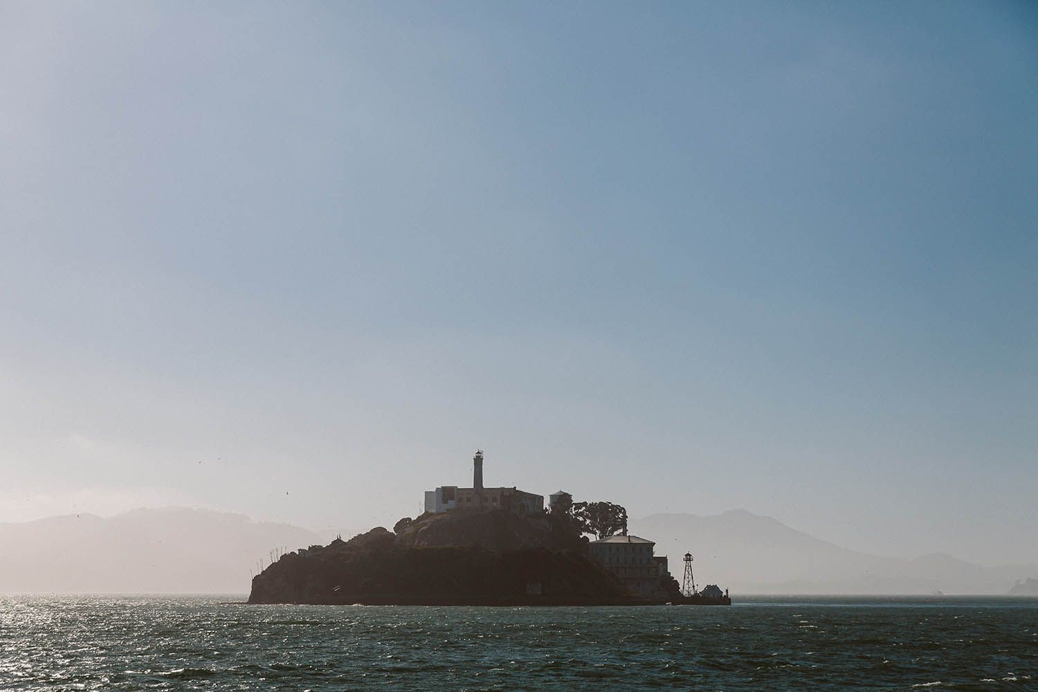 Color landscape photograph taken of Alcatraz in San Francisco showing the island sitting in the bay with blue sky above
