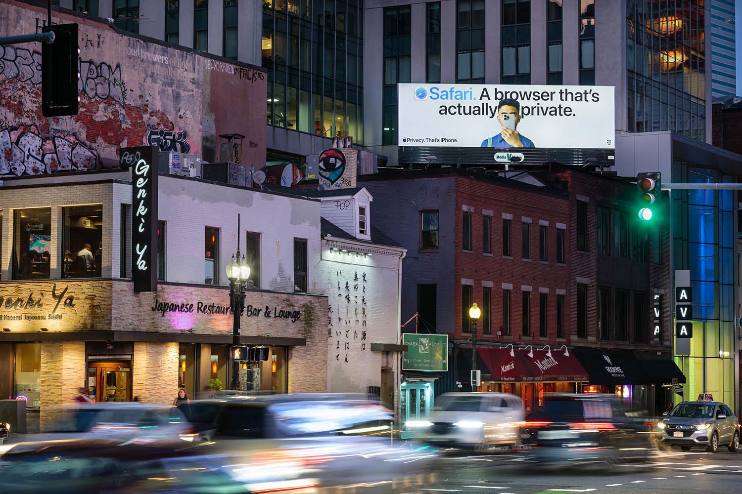 Architectural photograph of new Apple billboard posting taken at night in the city of Boston with cars driving past and movement on the road