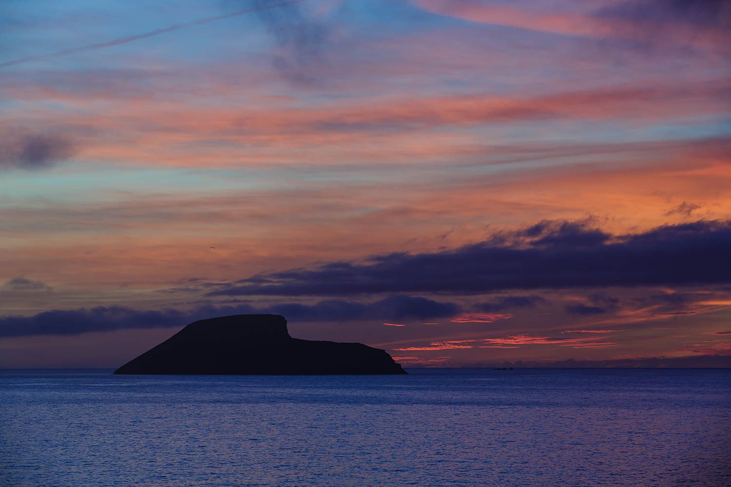 Color landscape photograph of Terceira Island in the Azores Portugal, showing small island off the coast at dusk with colorful sky and cloud
