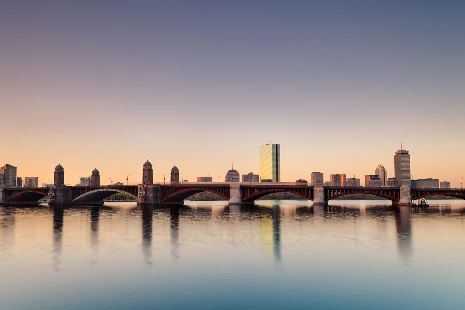 Color landscape photograph showing the Boston architectural skyline early in the morning and reflecting in the Charles River.