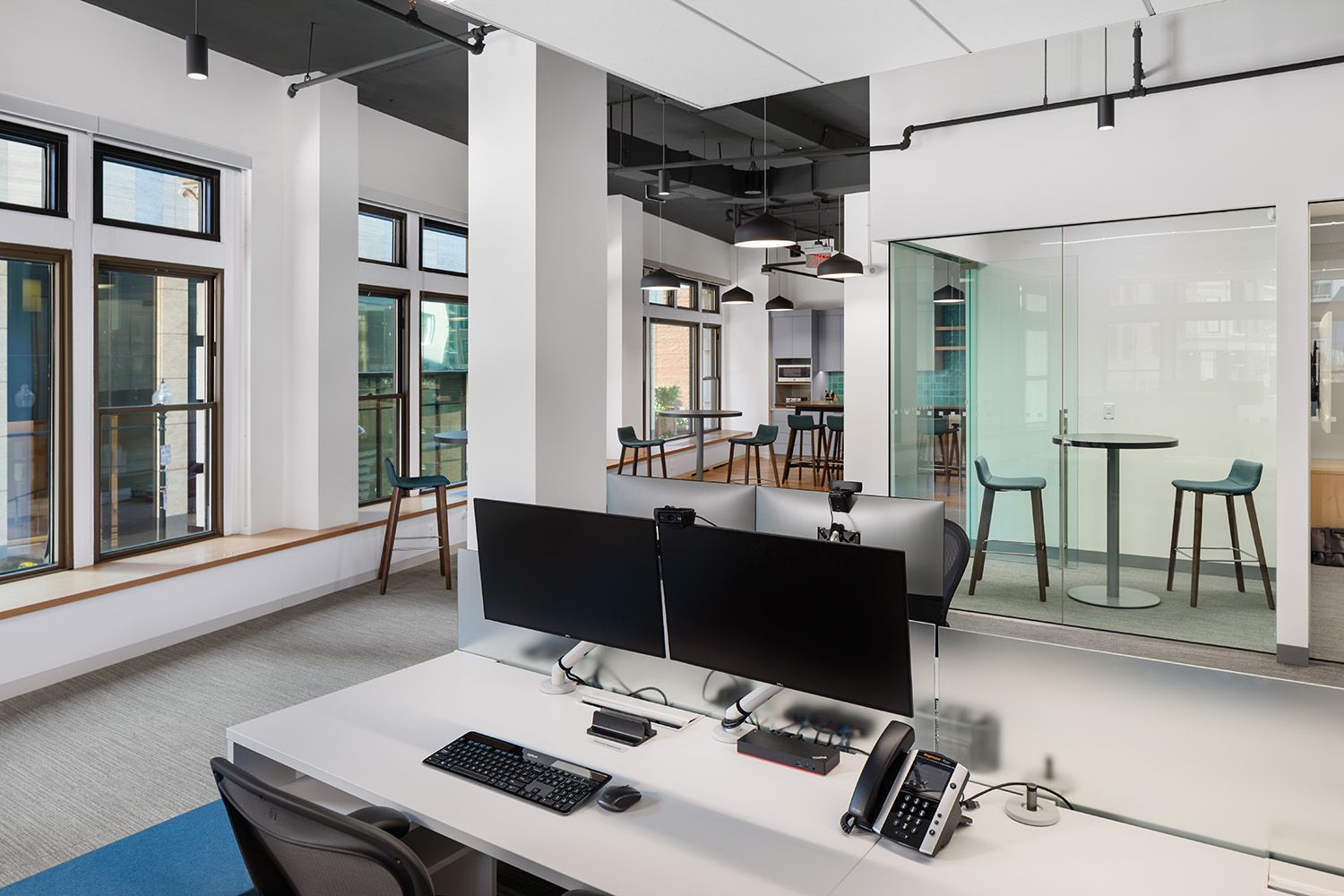A BRIGHT AND CHEERFUL WORKSTATION SET UP WITH SMALL MEETING ROOM FEATURED IN THE BACKGROUND IN A NEW BOSTON OFFICE LOCATION