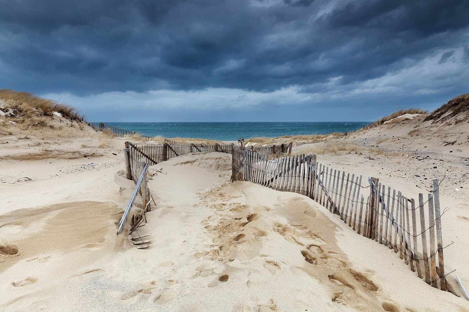 Deserted beach landscape photograph from Cape Cod during the winter months with very stormy sky over rough seas and sand dunes in foreground