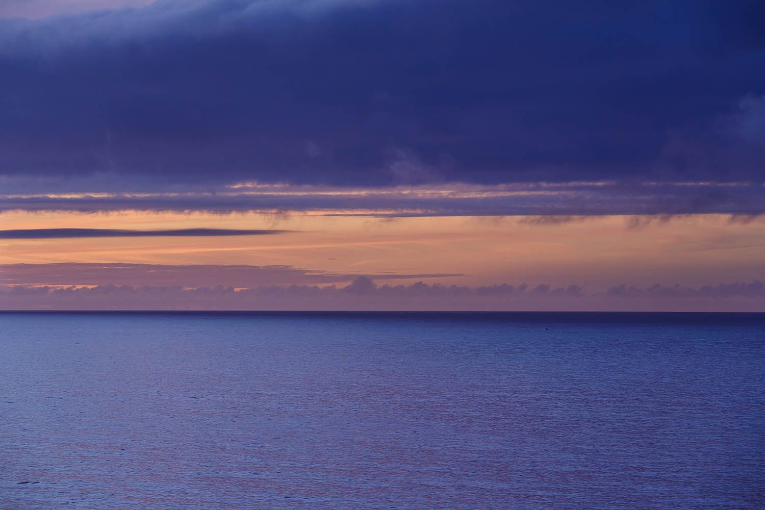 Color landscape photograph of Terceira Island, Azores Portugal, showing view out to sea at dusk with a band of colorful sky clouds above