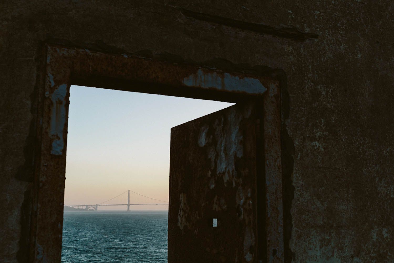 Color landscape photograph taken near San Francisco in California showing view of Golden Gate bridge from Alcatraz through a broken doorway
