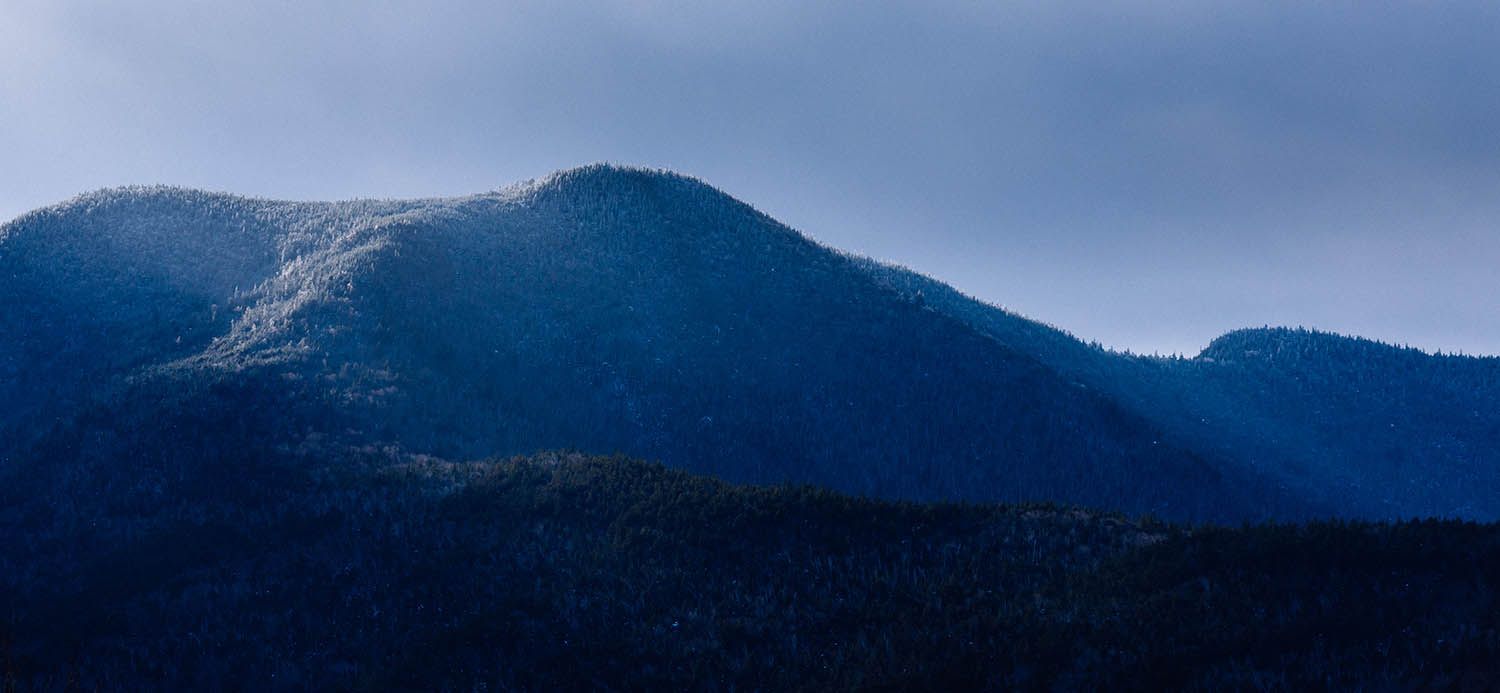 Winter landscape photograph taken in the White Mountain NH showing the sun hitting the side of snow cover trees at the top of mountain.