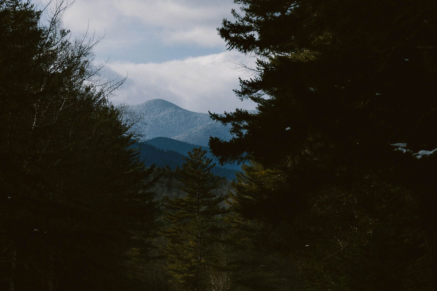 A winter mountain landscape photograph taken in NH White Mountain State Forest with mountain framed by tress on either side and stormy sky