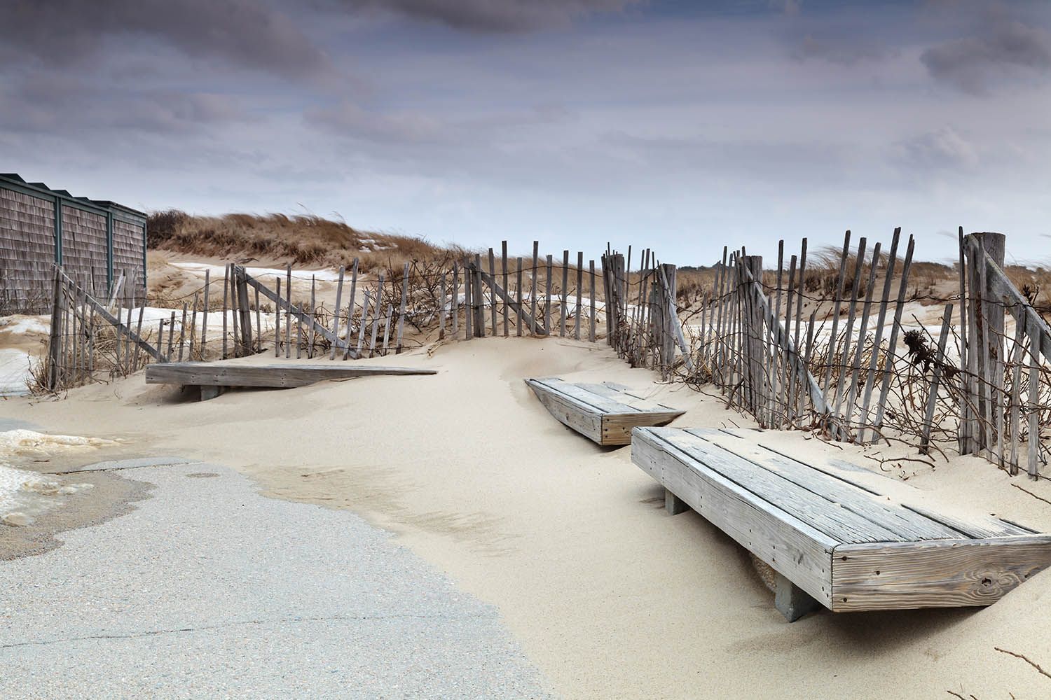 Winter beach landscape photograph in color of sand piling up around benches that have been deserted