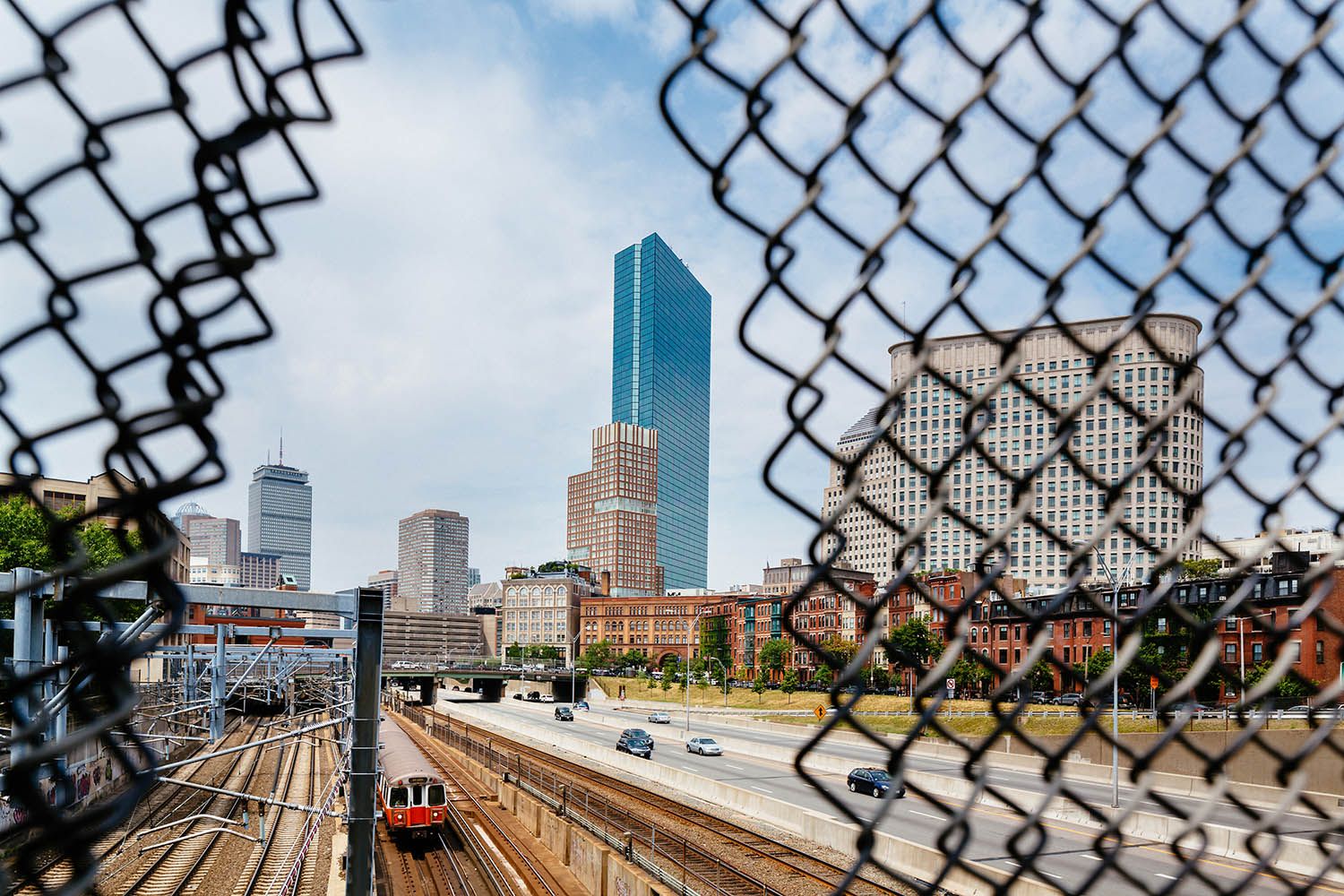 Color landscape photograph Boston skyline taken through a broken fence gap and trains in the foreground on a nice summers day