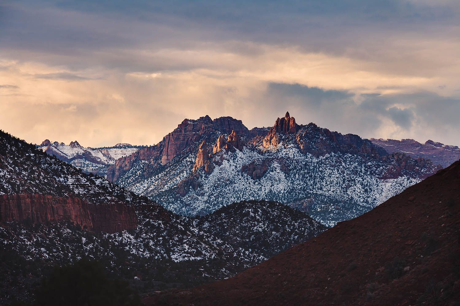 Color landscape photograph of wintery mountain scene in Zion Utah taken at dusk with colorful sky over mountain range and snow showing