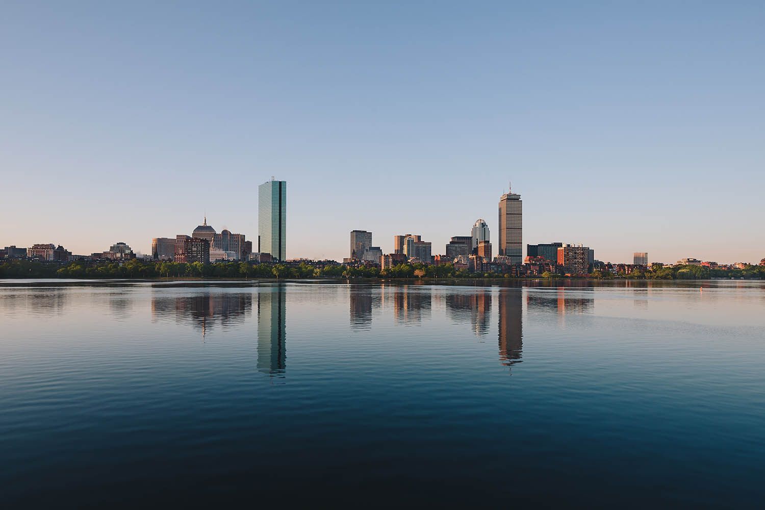 Color landscape photograph showing the Boston architectural skyline early in the morning and reflecting in the Charles River.