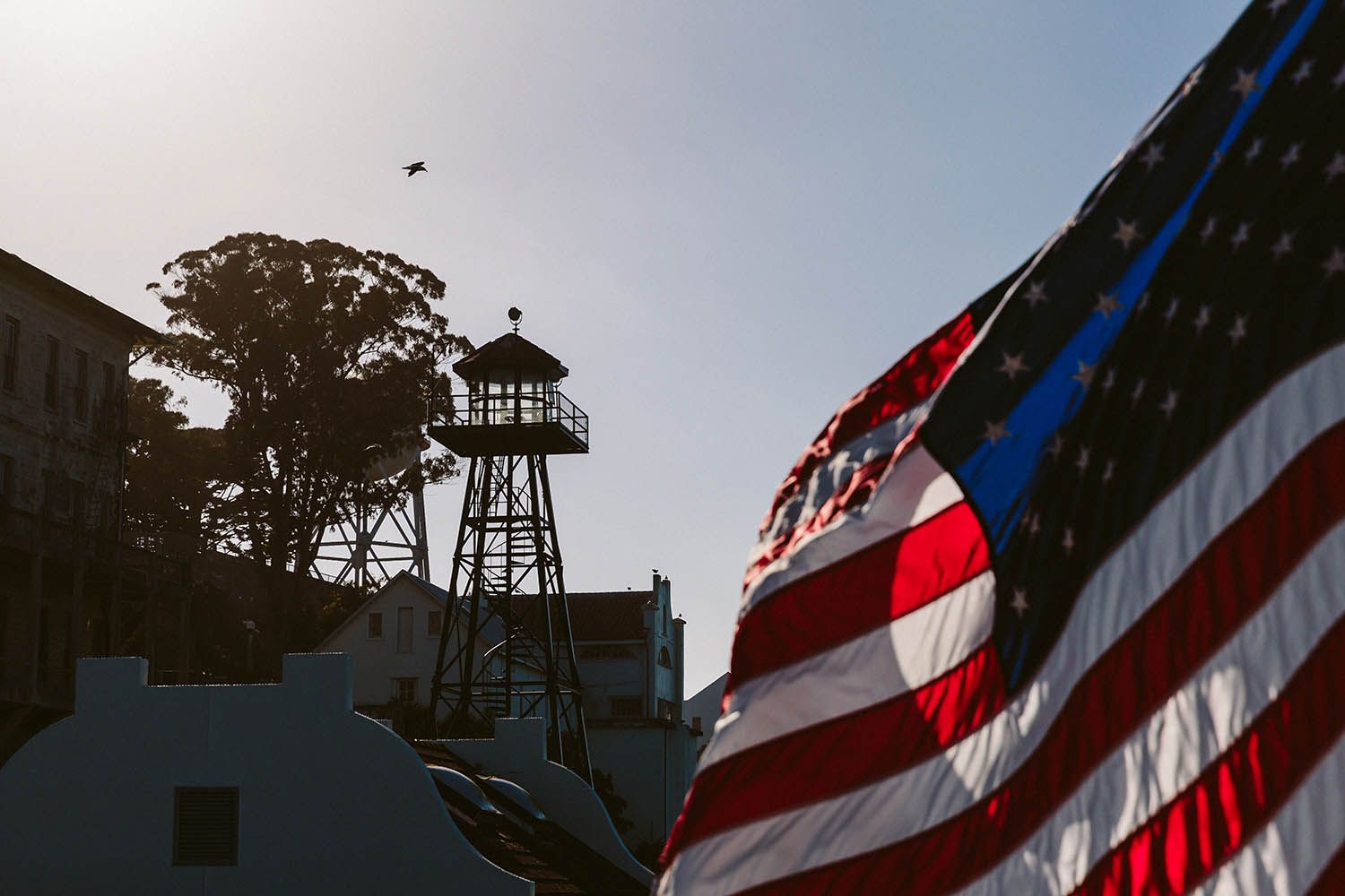 Color landscape photograph taken from Alcatraz in San Francisco showing America flag and watch tower with seagulls flying in the air