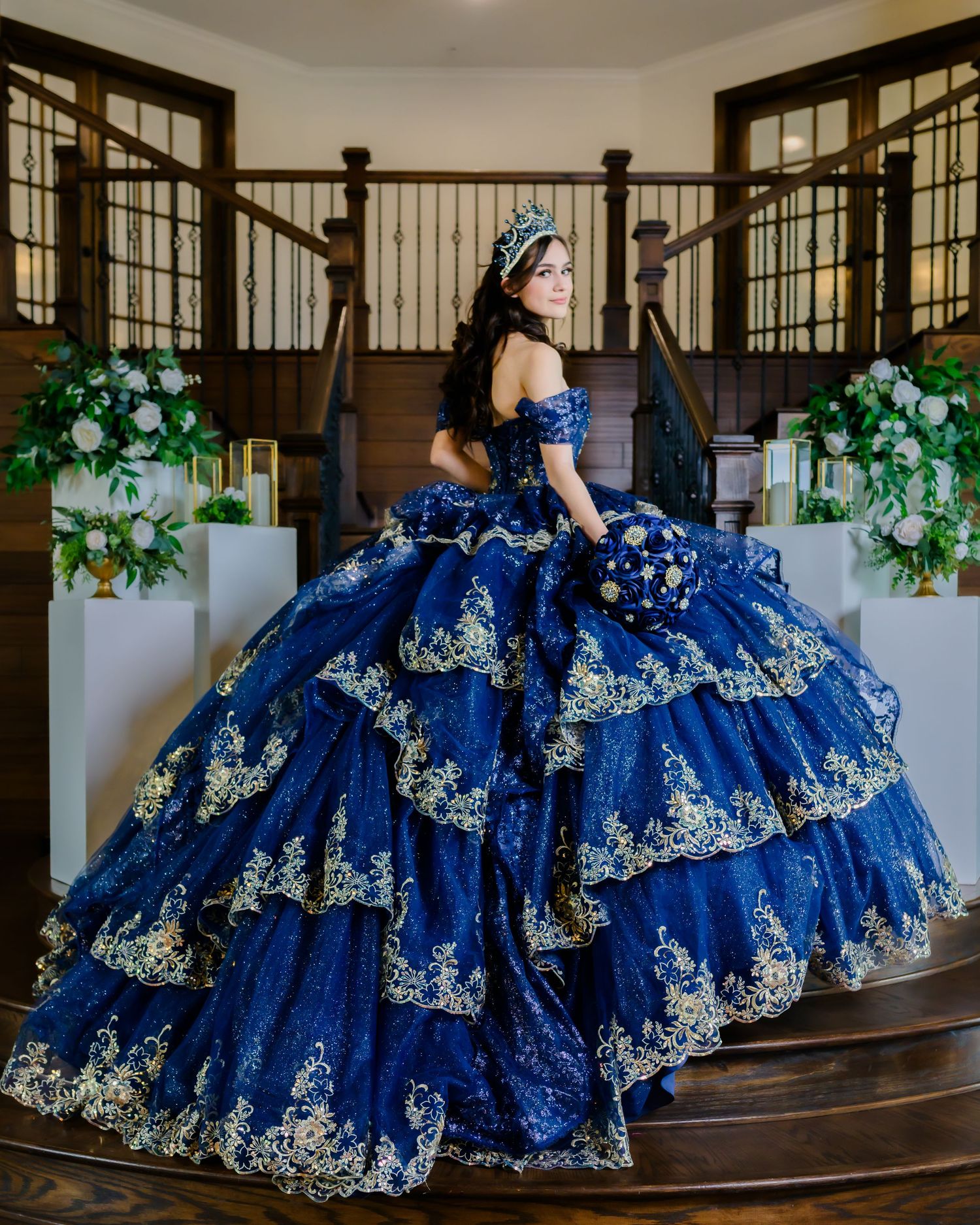 Stunning royal blue quinceañera dress with elaborate silver embroidery showcased on staircase in multiple elegant poses.