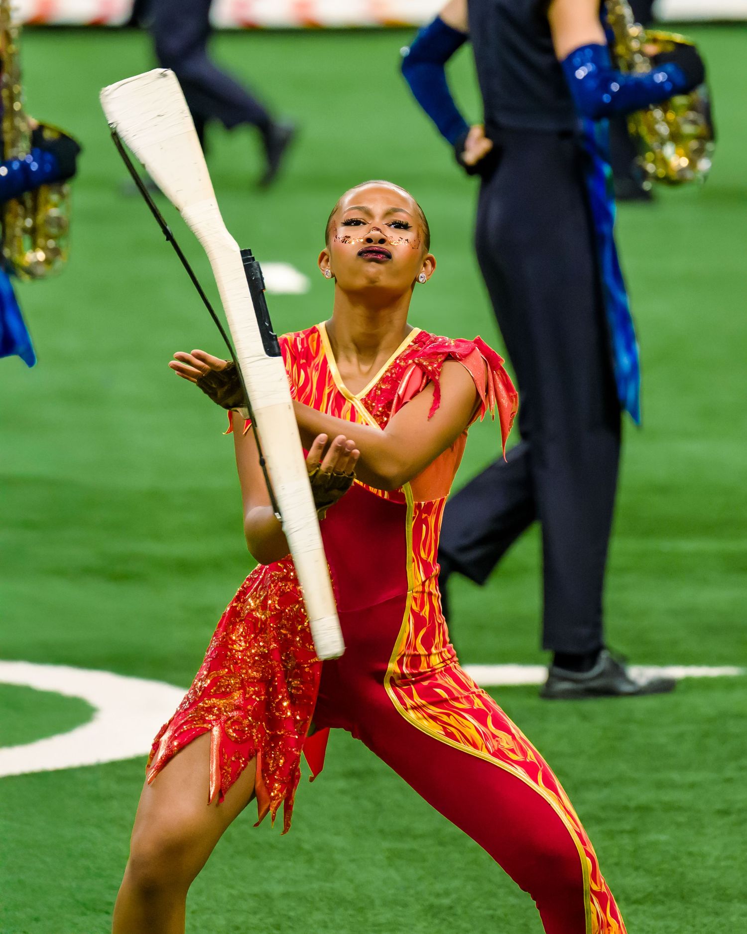 Baton twirler in red and gold costume performs energetic routine during halftime show on football field.