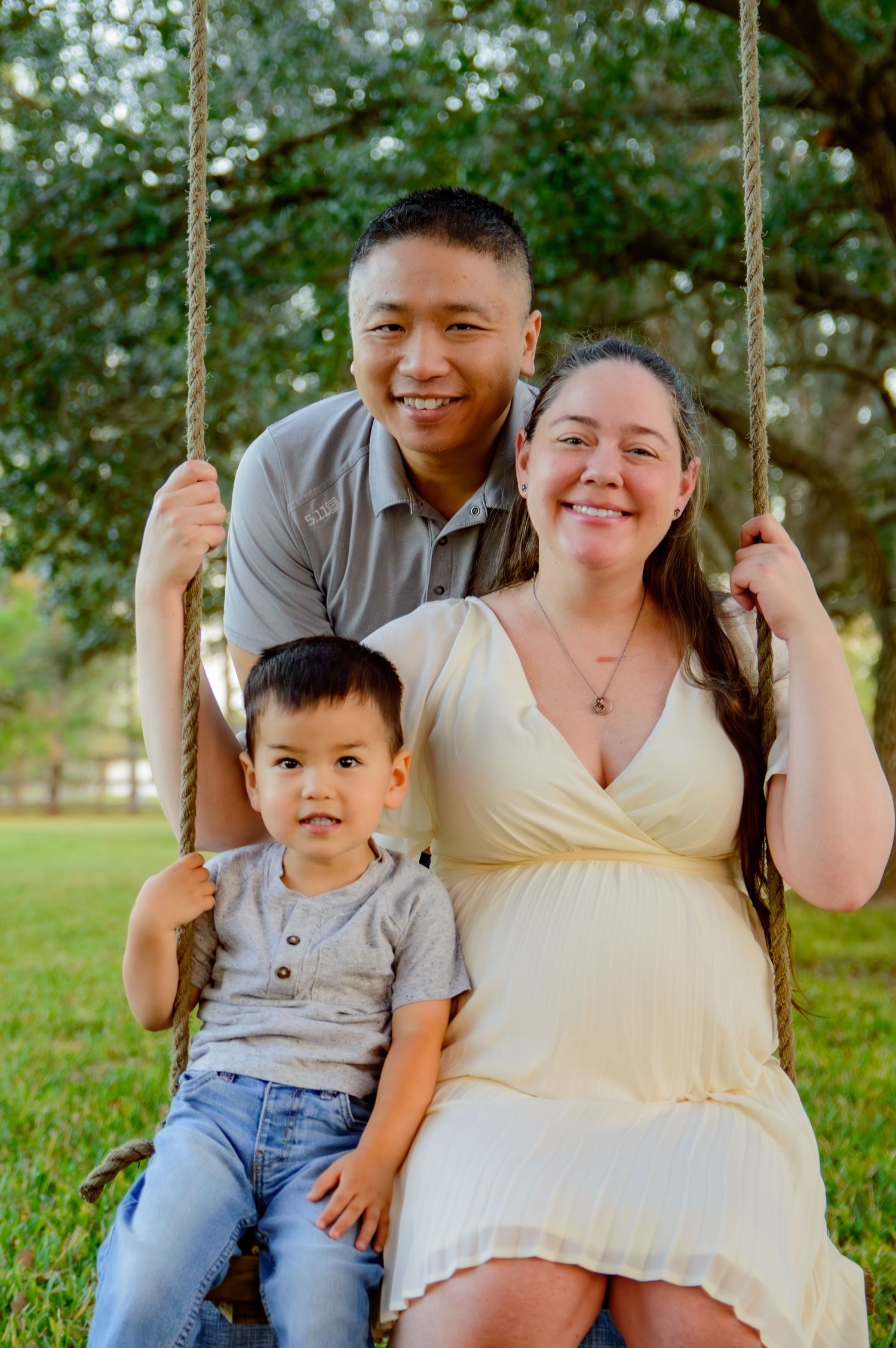 Romantic outdoor portrait session at a park with couple and child sitting together on a tree swing on sunny day.
