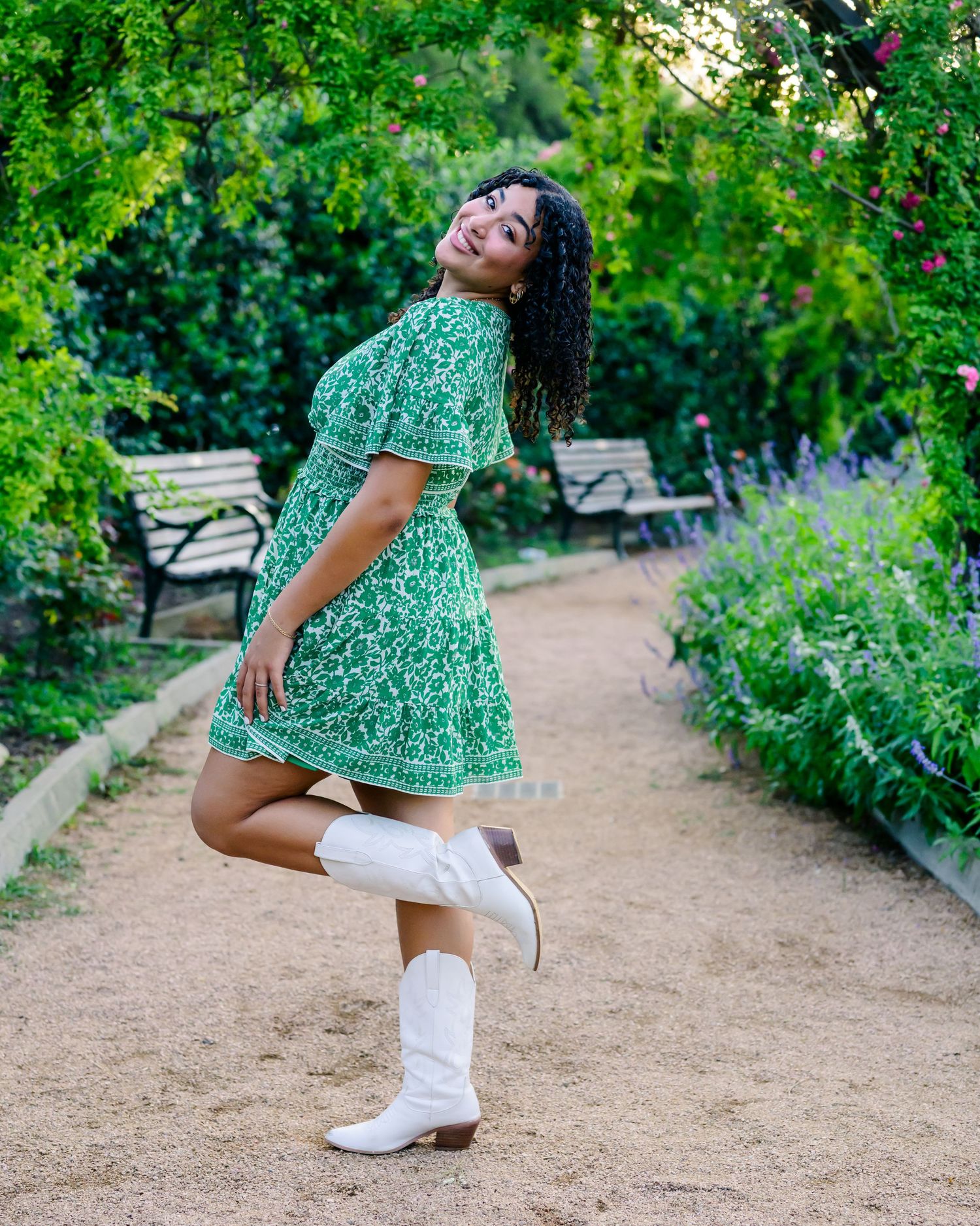 Dancing along a garden path in a green floral dress, white cowboy boots, and carefree laughter among blooming flowers.