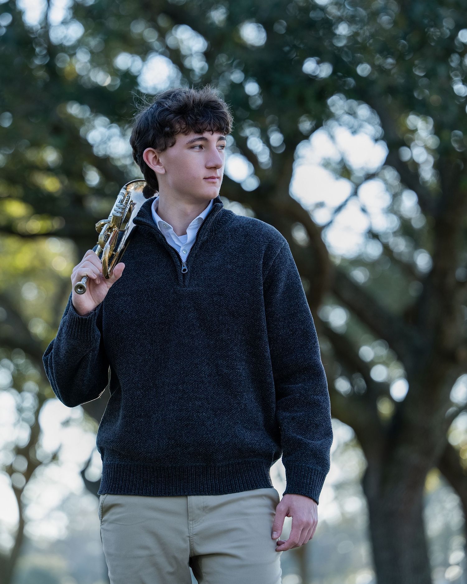 A person in a dark sweater and khaki pants stands outdoors against a blurred forest background.