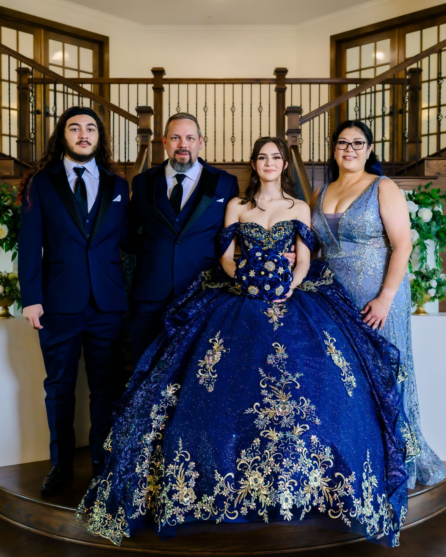 Family group in formal attire with stunning royal blue and gold quinceañera ball gown at an elegant venue.