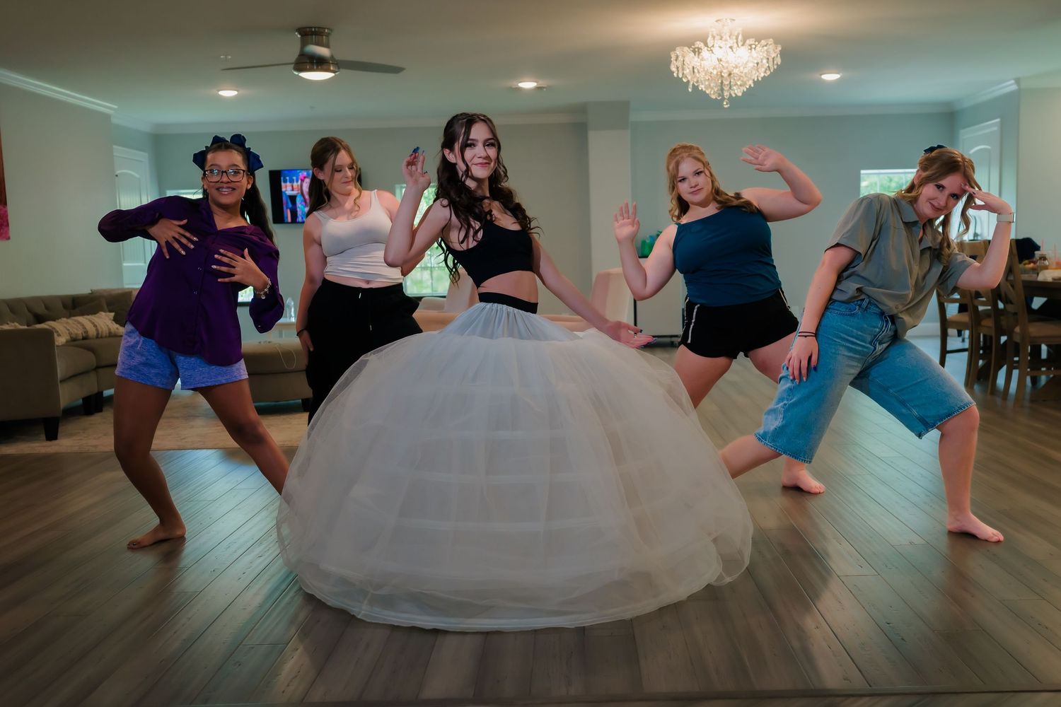 A group of people dancing and posing playfully around someone wearing a dramatic white ballgown with a full skirt.
