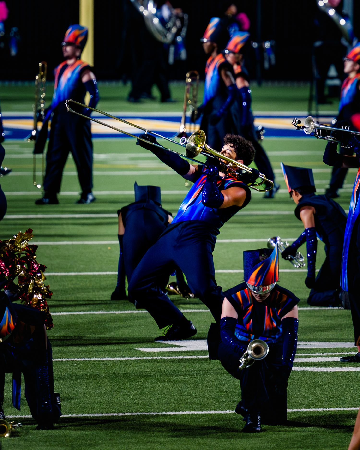 Marching band members perform a synchronized move while playing instruments on a football field during a performance.