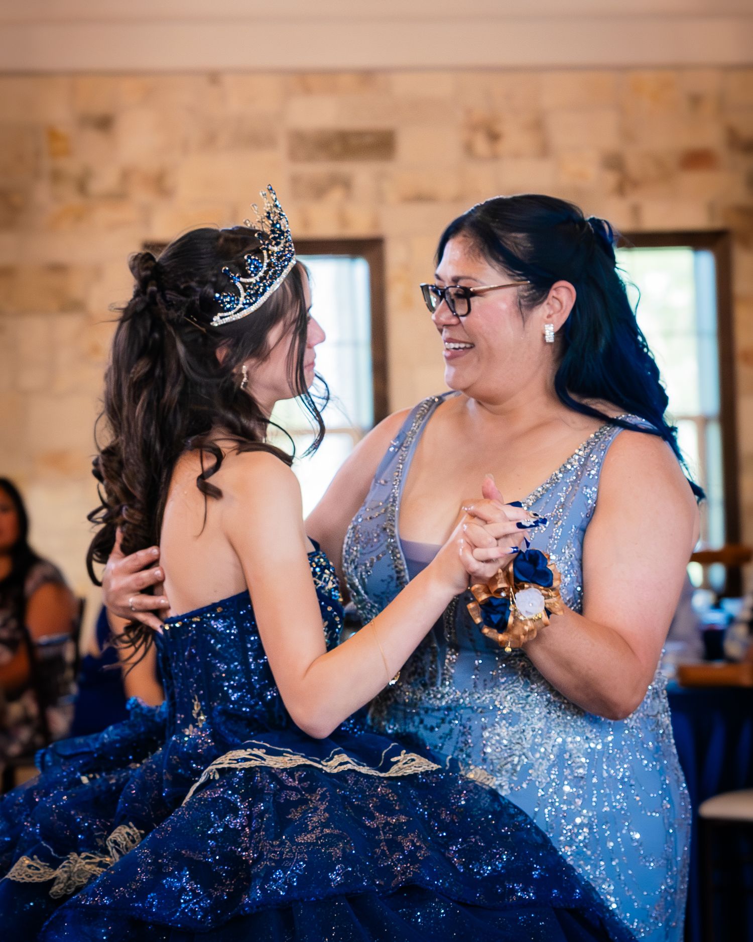 Two people wearing sparkly blue dresses share an intimate dance moment at an indoor celebration.